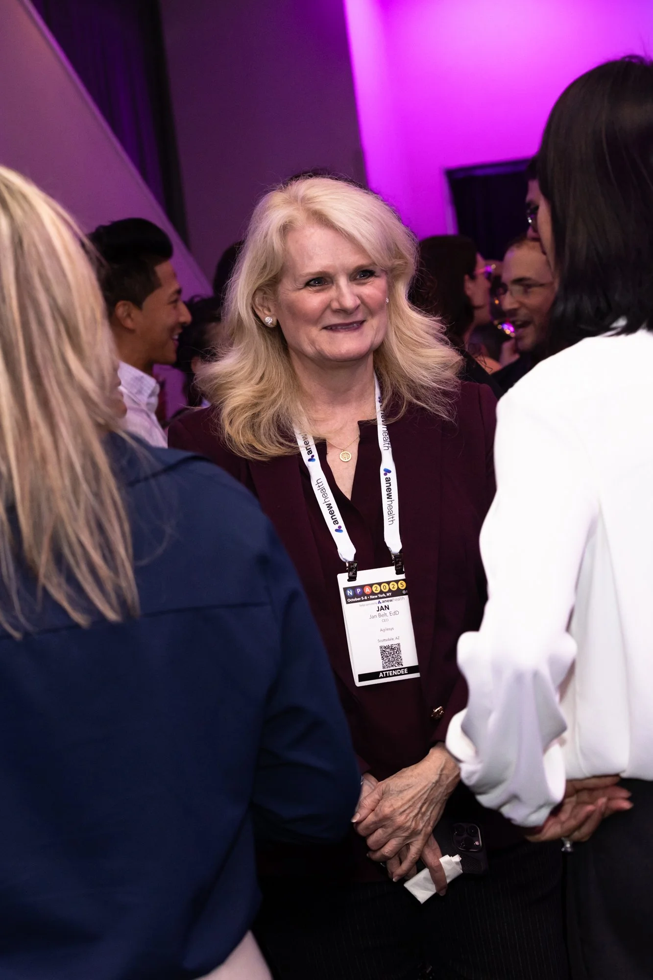 A group of people at a conference, with one woman with long blonde hair smiling and wearing a conference badge around her neck.