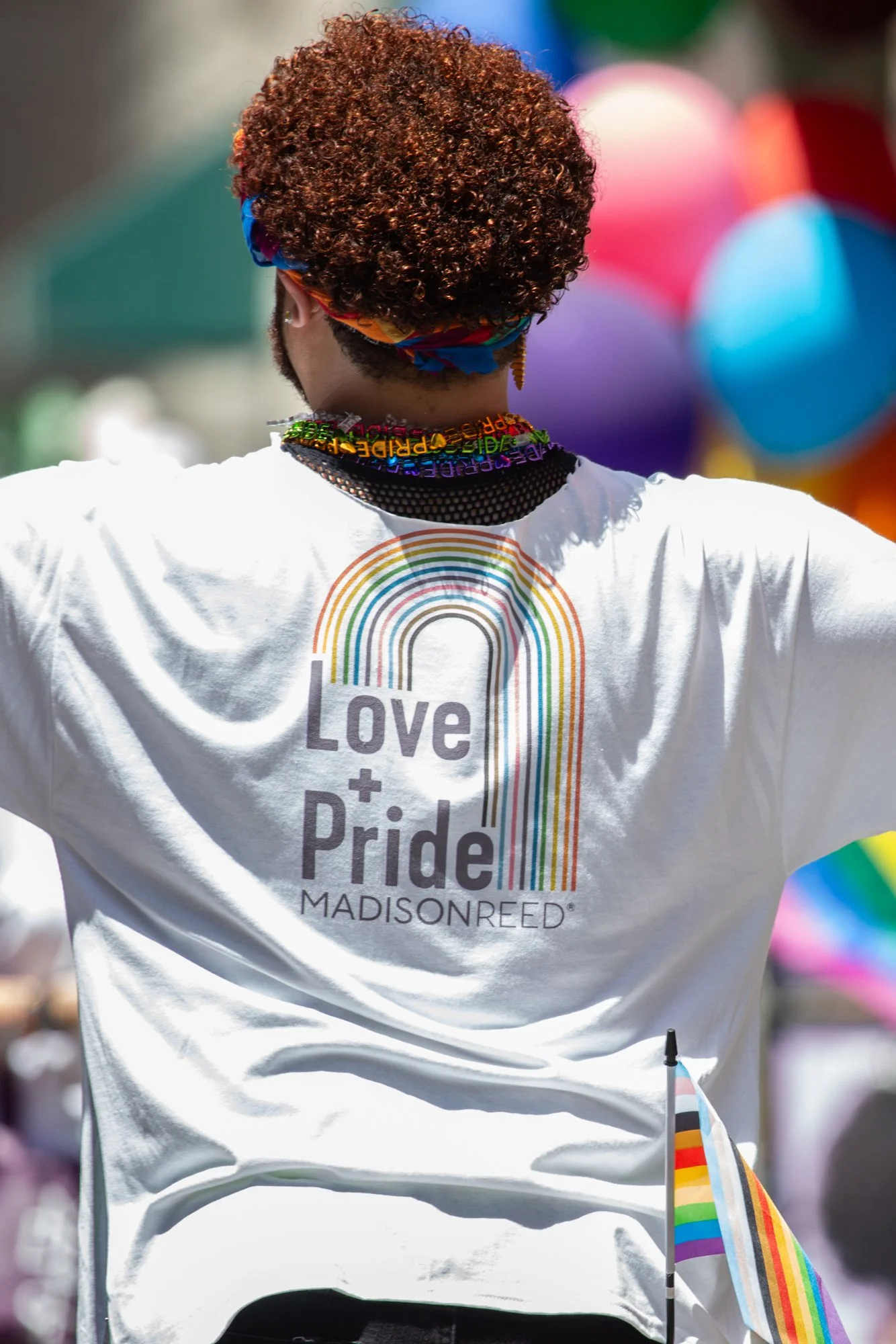 Person wearing a Love + Pride Madison Reed shirt and rainbow accessories at a Pride celebration