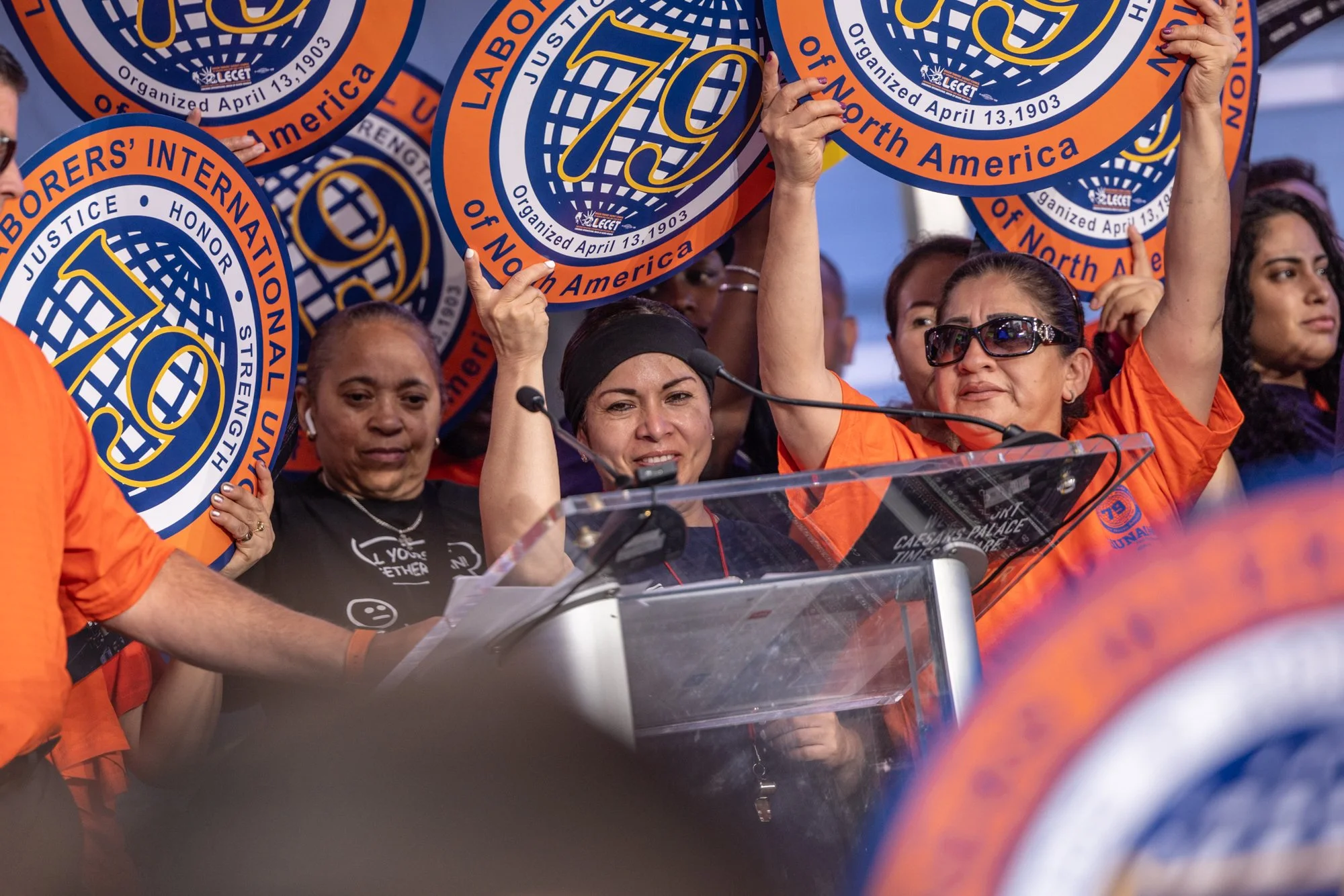 People holding up signs with the logo and name of the organization UNITE HERE, indicating a gathering or protest.
