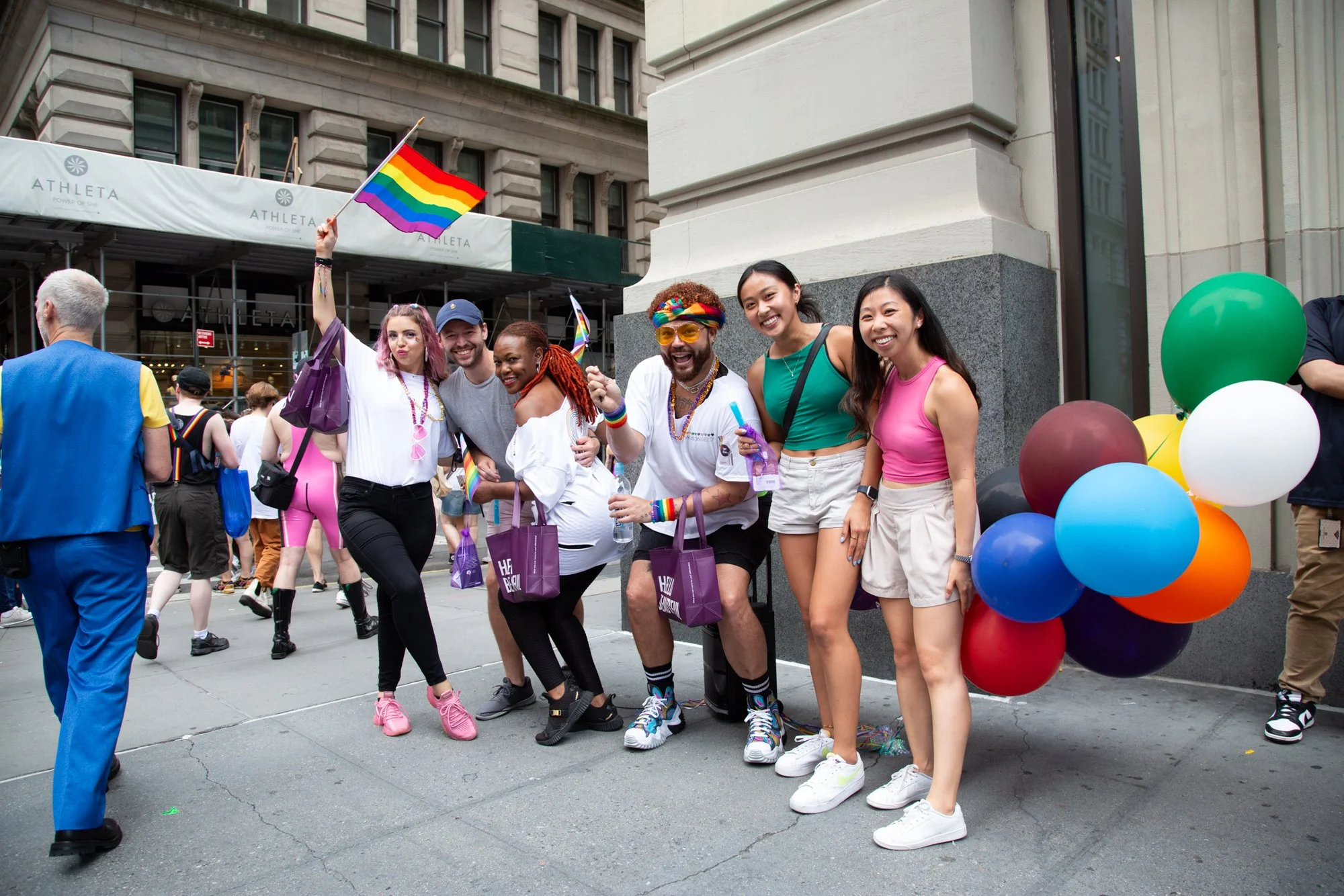 Group celebrating at a Pride parade with rainbow flags and colorful balloons outside a city building
