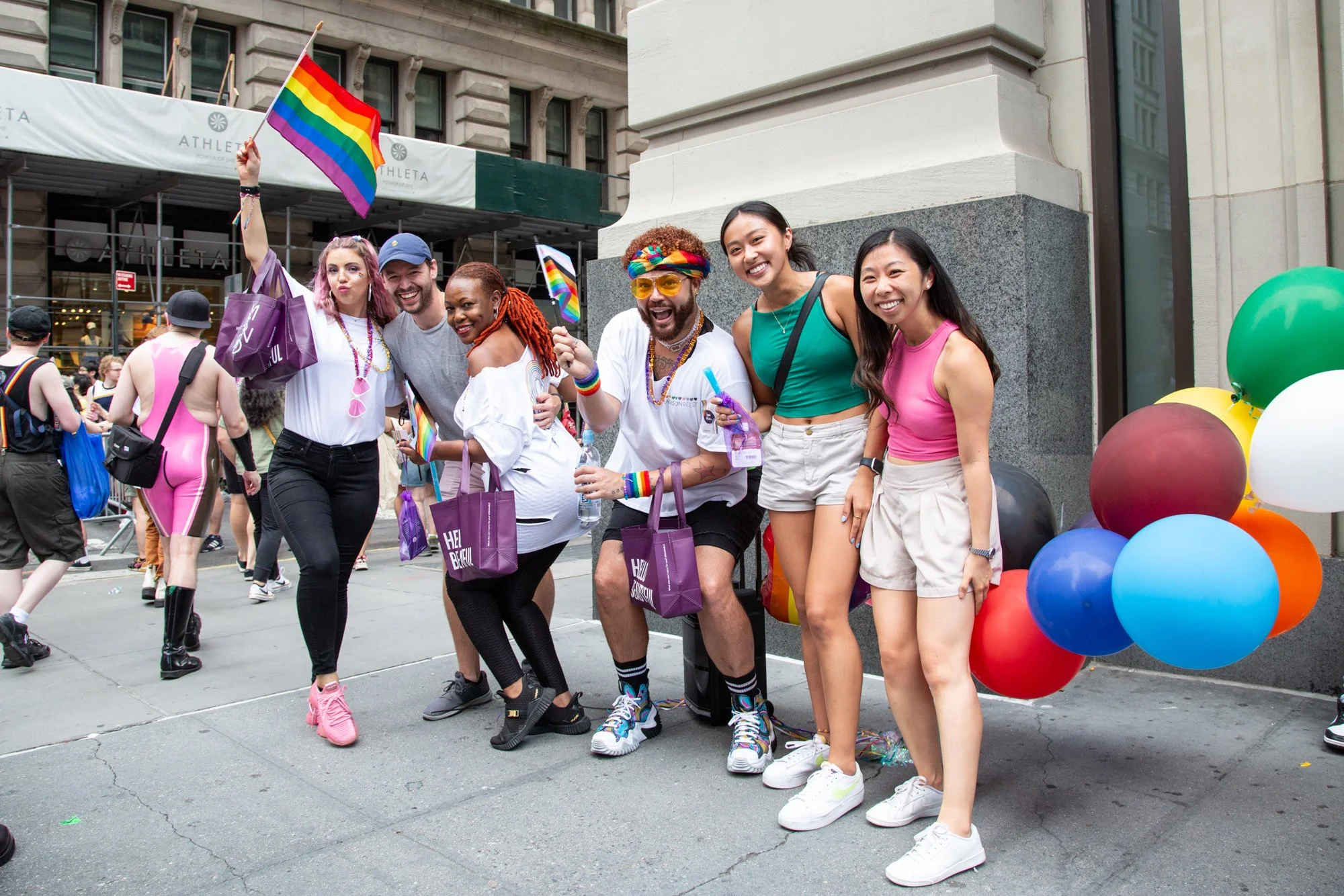 Group of people celebrating Pride outdoors with rainbow flags and colorful balloons