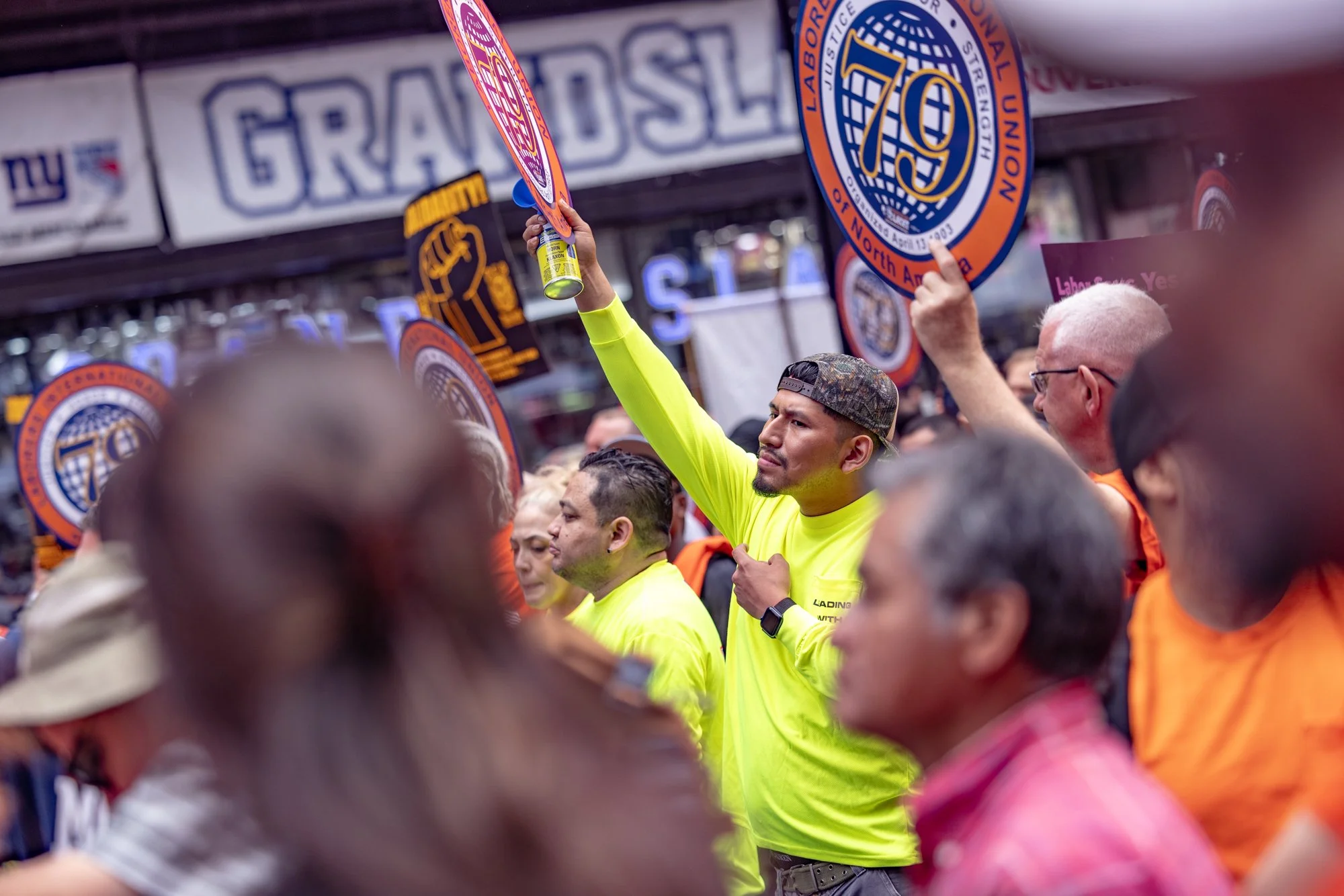 Crowd of people gathered at a celebration or rally, with some holding signs and banners, including one prominently displaying the number 70, indicating a 70th anniversary or milestone celebration.