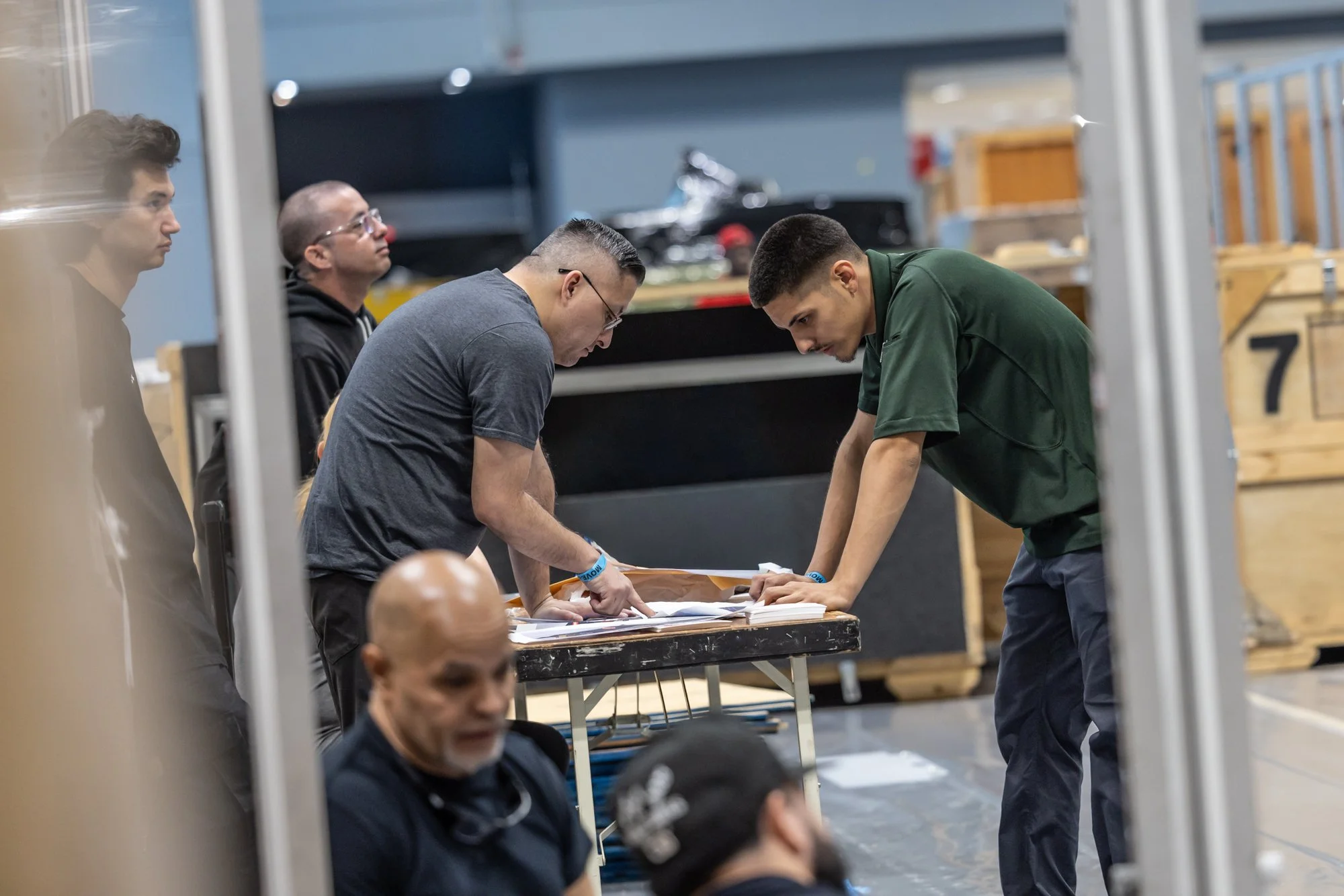 Production crew members review paperwork on a worktable backstage among equipment crates.