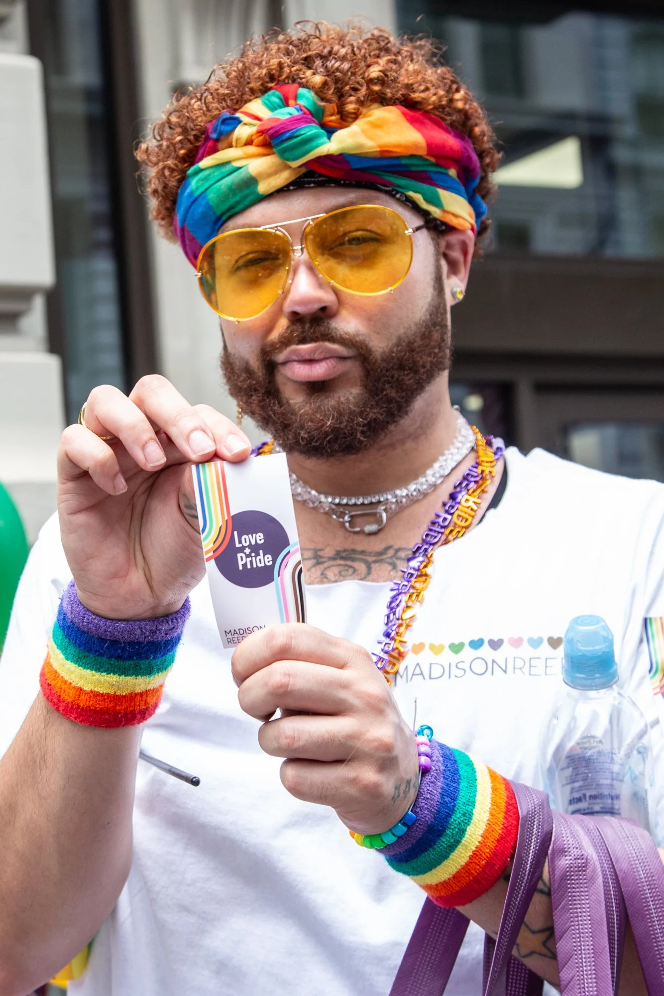 Person wearing a rainbow headband, yellow sunglasses, Pride accessories, and a Love + Pride card at a Pride celebration