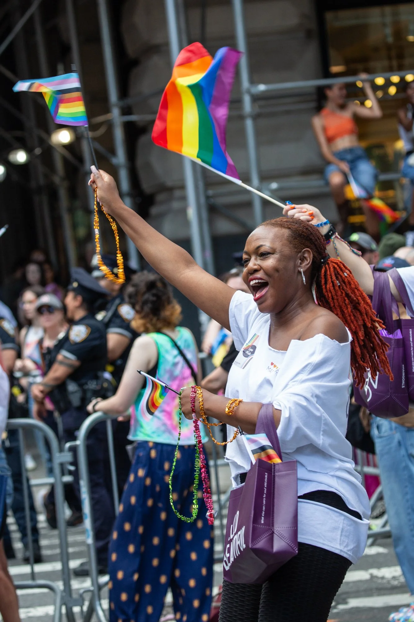 Woman celebrating at a Pride parade while waving a rainbow flag and wearing colorful beads.