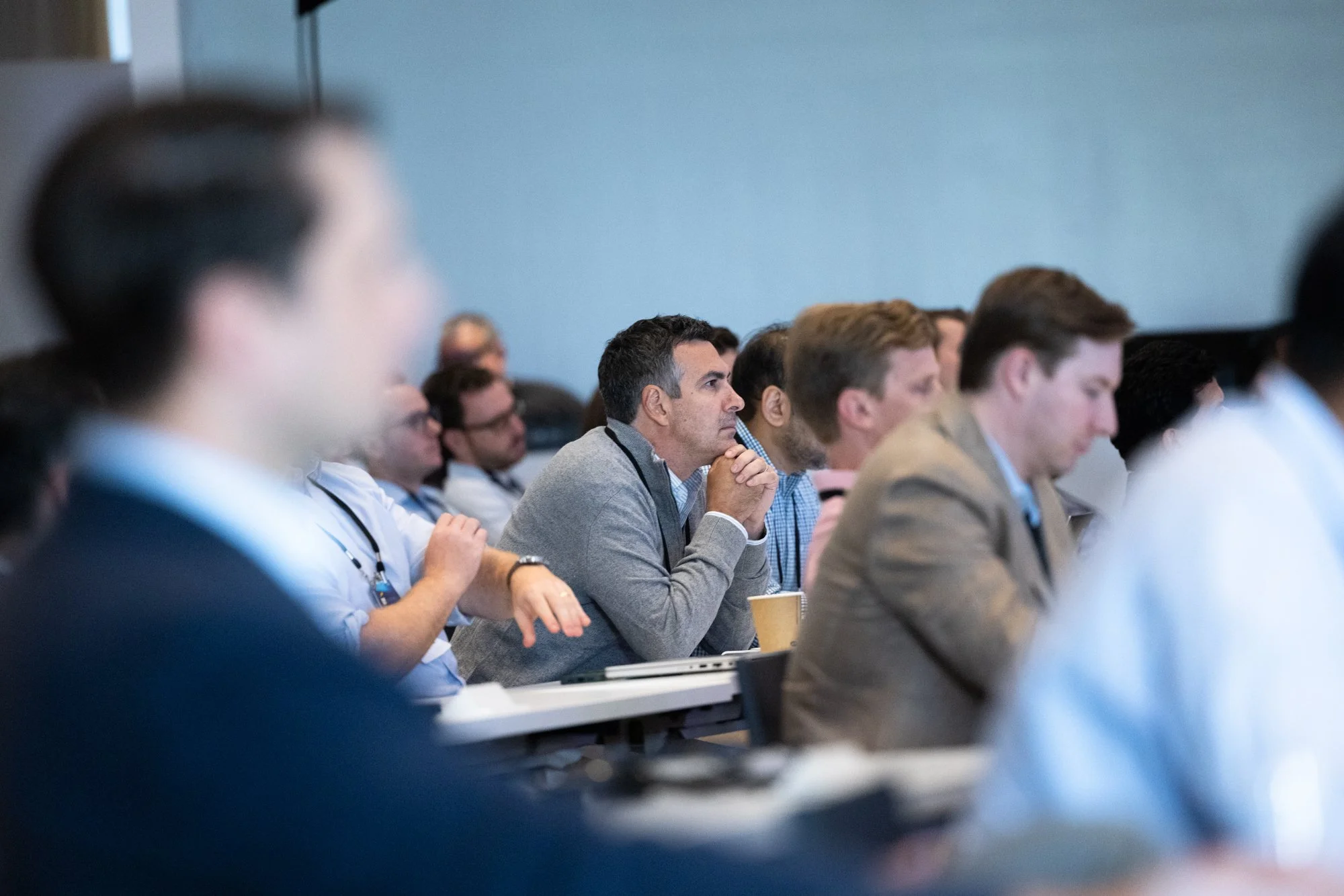 Group of people attending a conference or seminar, sitting at tables and listening attentively.