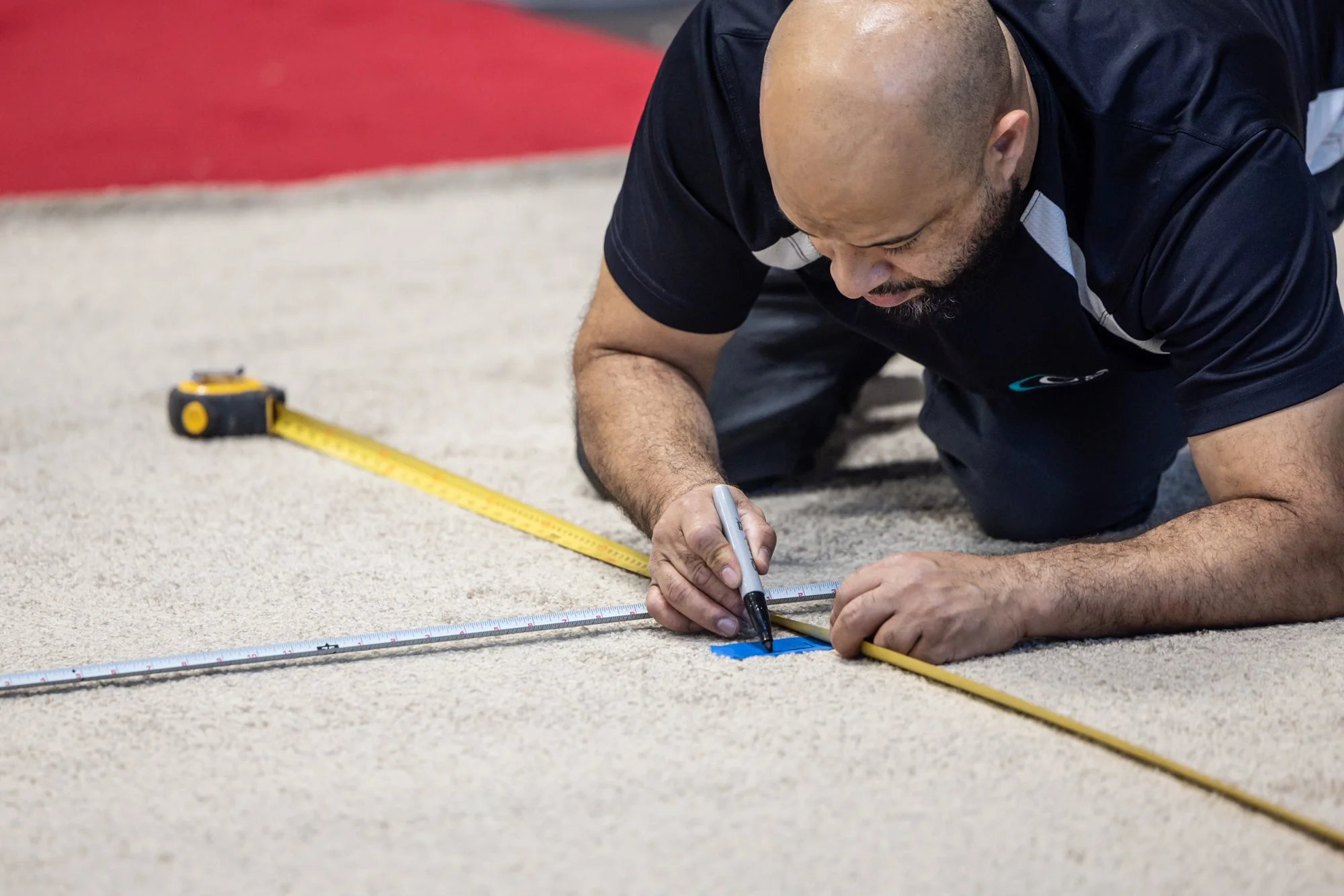 Man measuring and marking a concrete floor with a tape measure, ruler, and marker