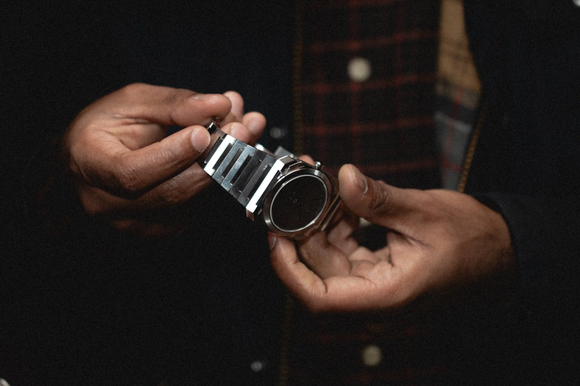 A person adjusting a silver wristwatch with a metal band on their wrist, with a dark background.