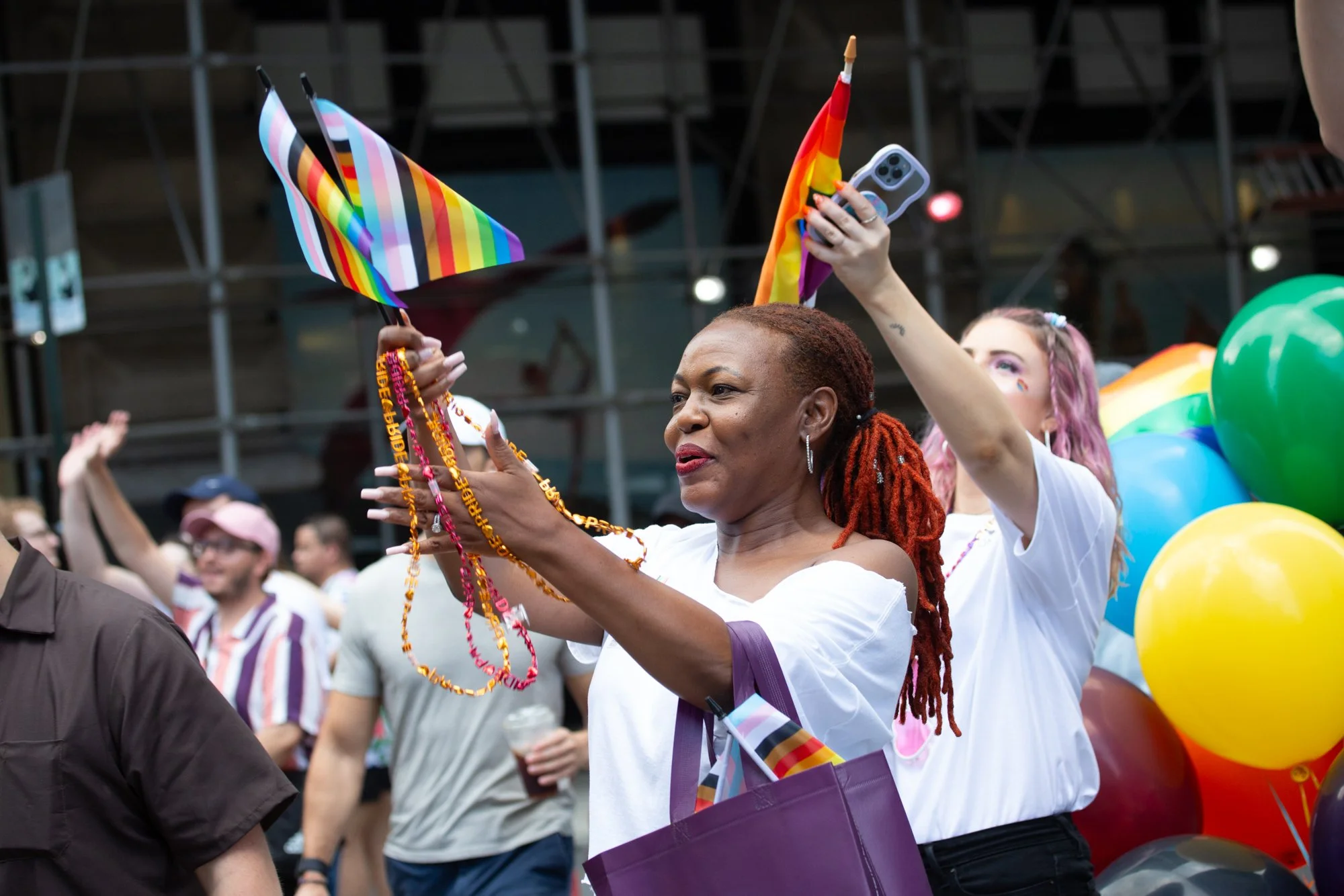Crowd celebrating at a Pride parade with rainbow flags, balloons, and colorful outfits