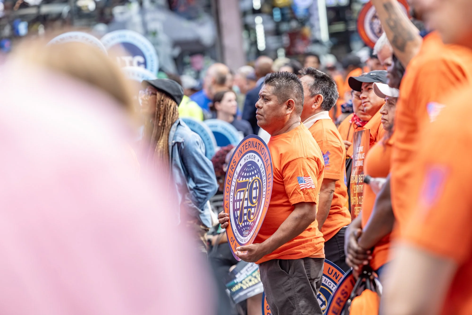 A group of people dressed in orange shirts participating in a public gathering or protest, holding signs and standing in a line.