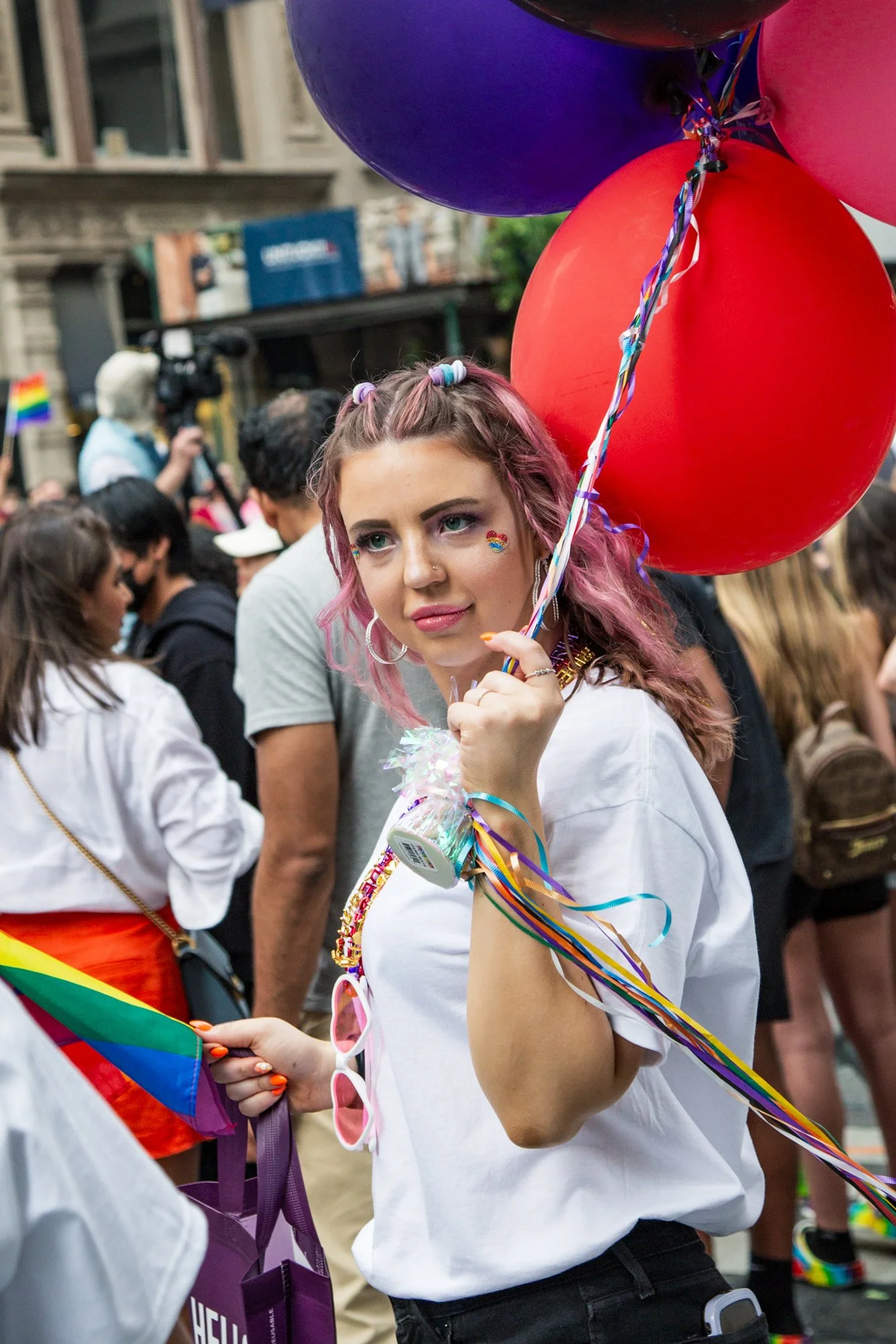 Woman with pink hair holding colorful balloons and a rainbow flag at a Pride parade