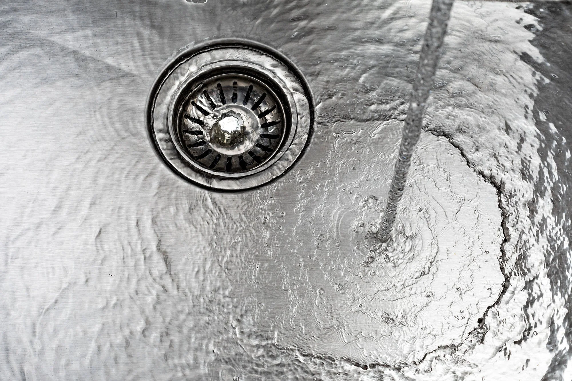 A stainless steel sink with water running into it, creating ripples and bubbles around the drain.