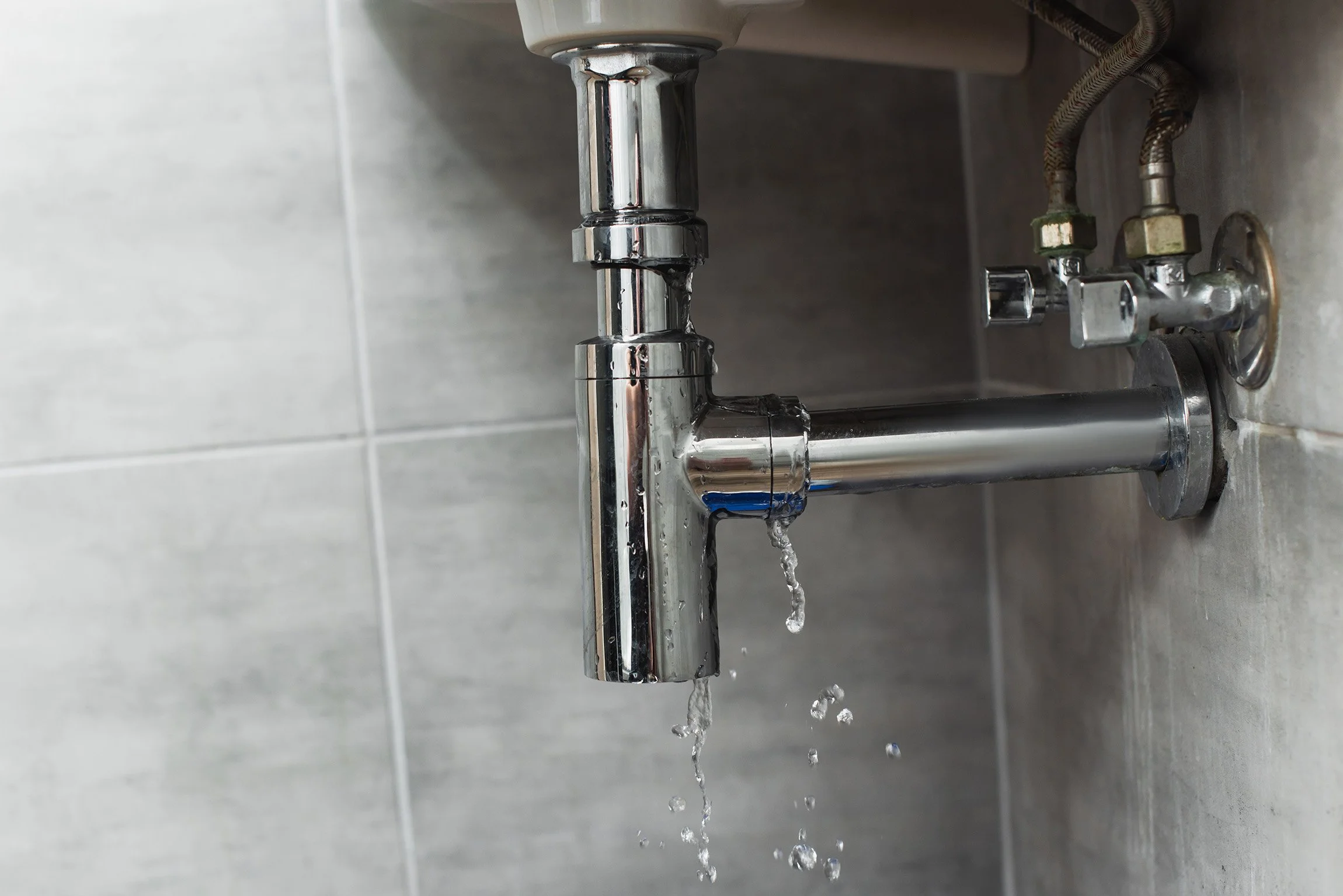 Close-up of a chrome sink faucet with water flowing out, mounted on a tiled wall.