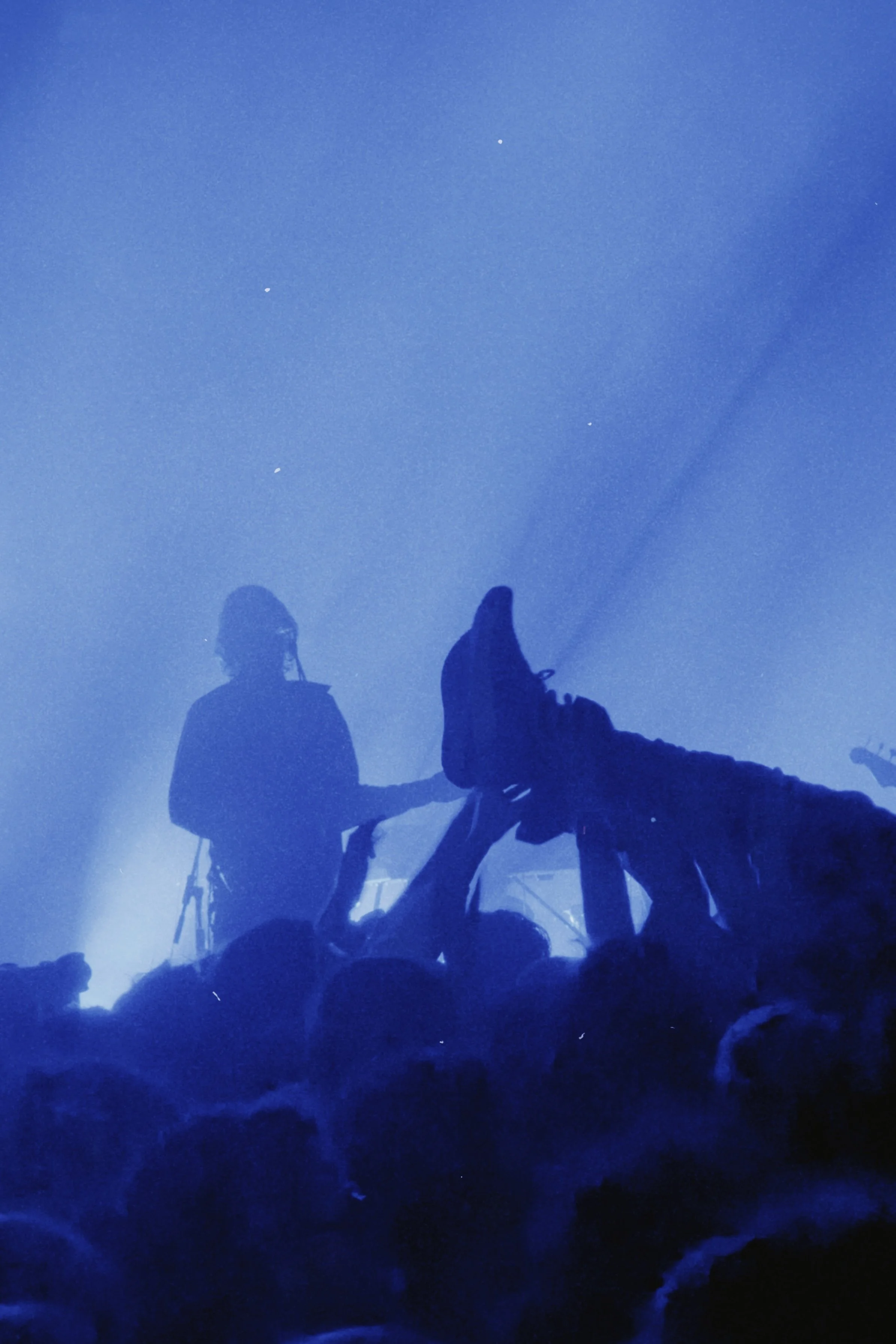 People in silhouette riding horses in a misty, dark blue landscape.