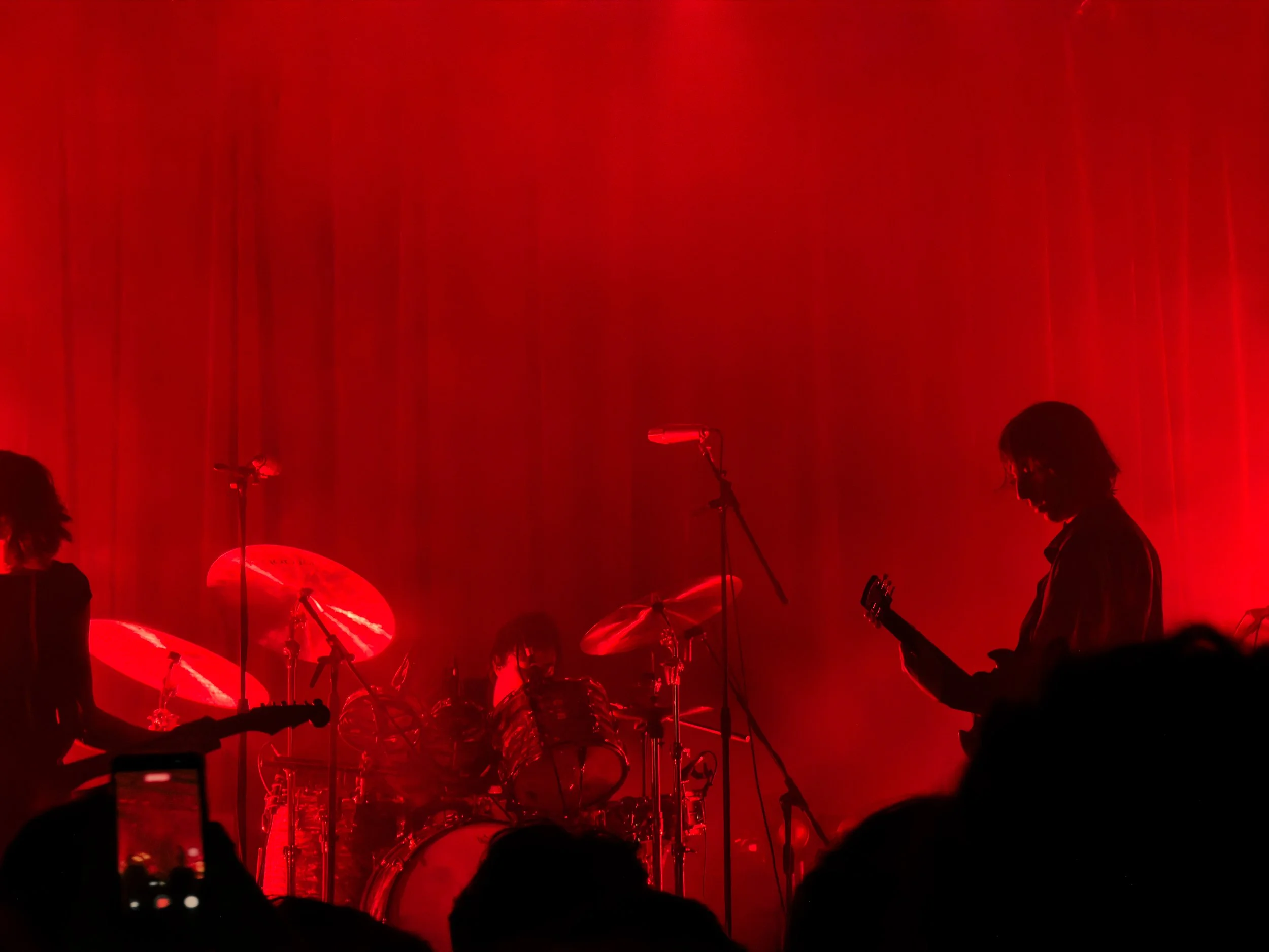 A band performing on stage illuminated in red light, with silhouettes of musicians playing instruments and microphones visible.
