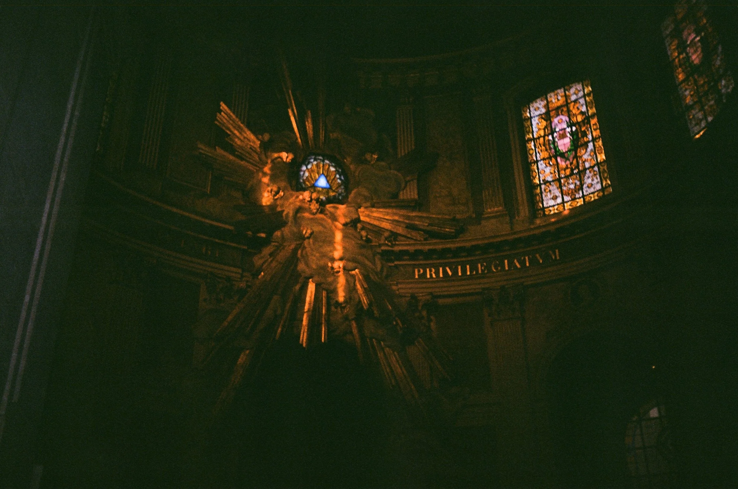 Dimly lit church interior with stained glass windows and the word 'PRIVILEGIUM' on a gold banner.
