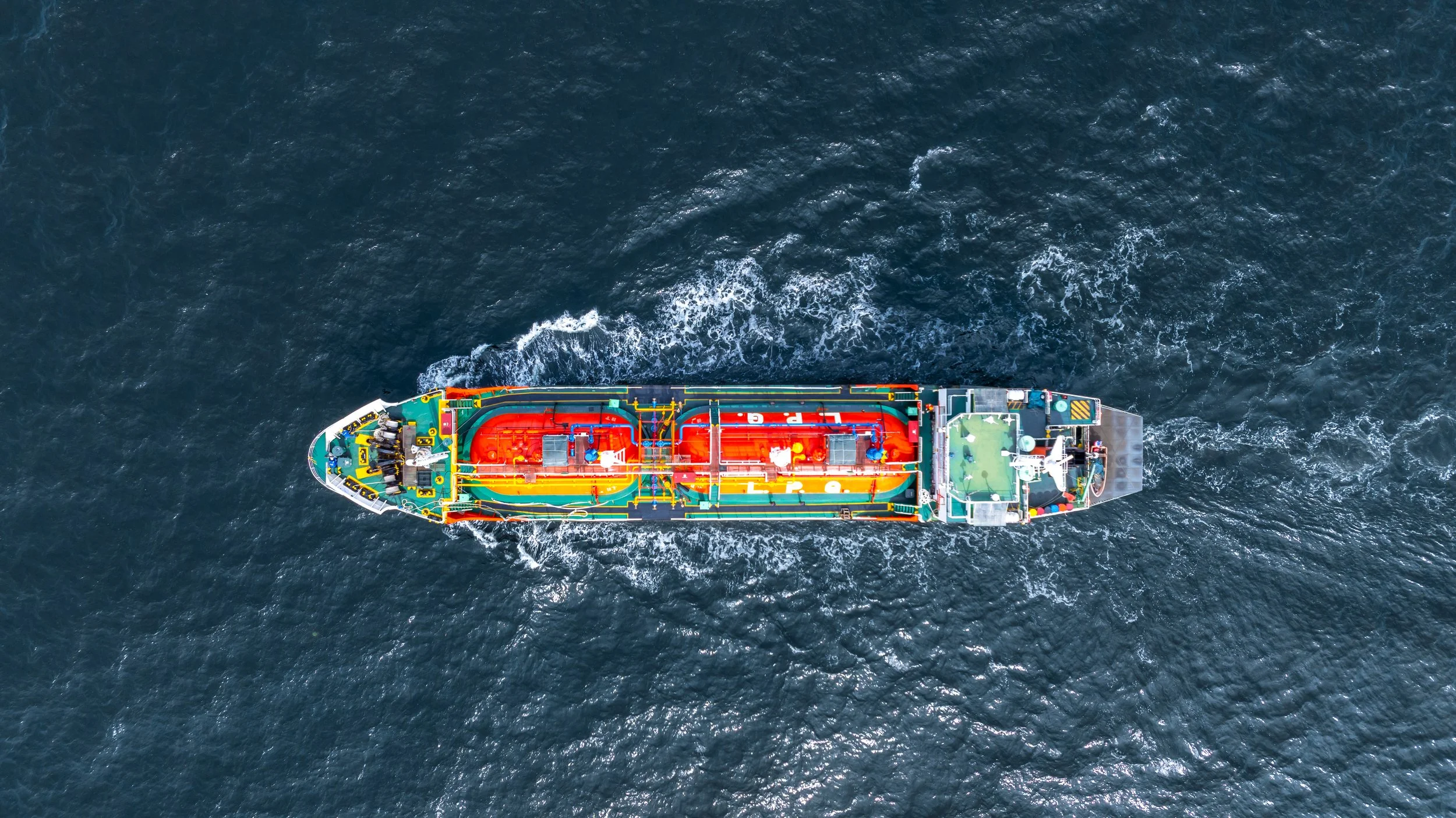 An aerial view of a colorful maritime vessel moving through darkblue ocean water.