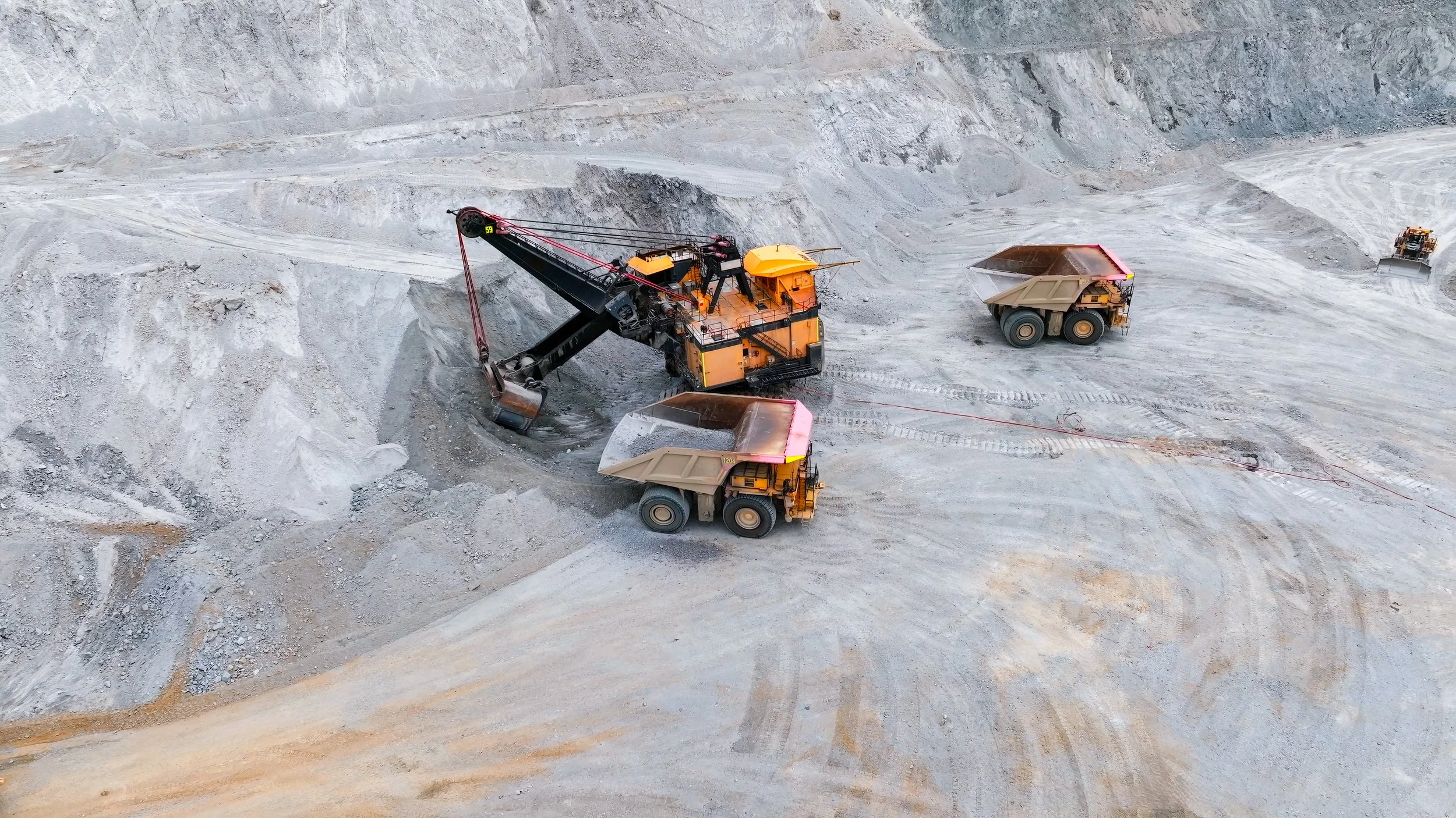 Mining operation with large excavator and dump trucks at a quarry or mine site.