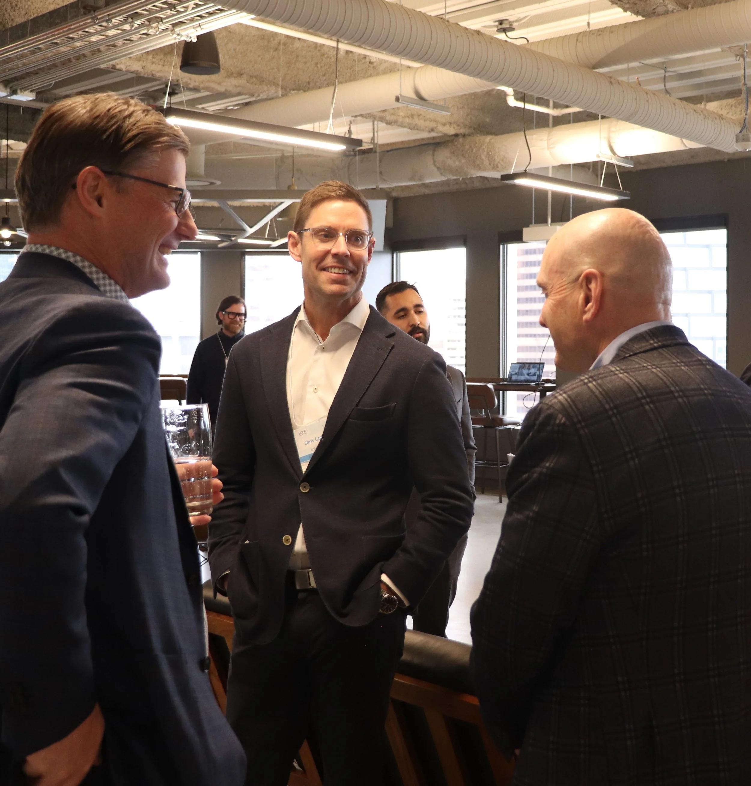 Group of men in business attire engaging in conversation at an indoor networking event.