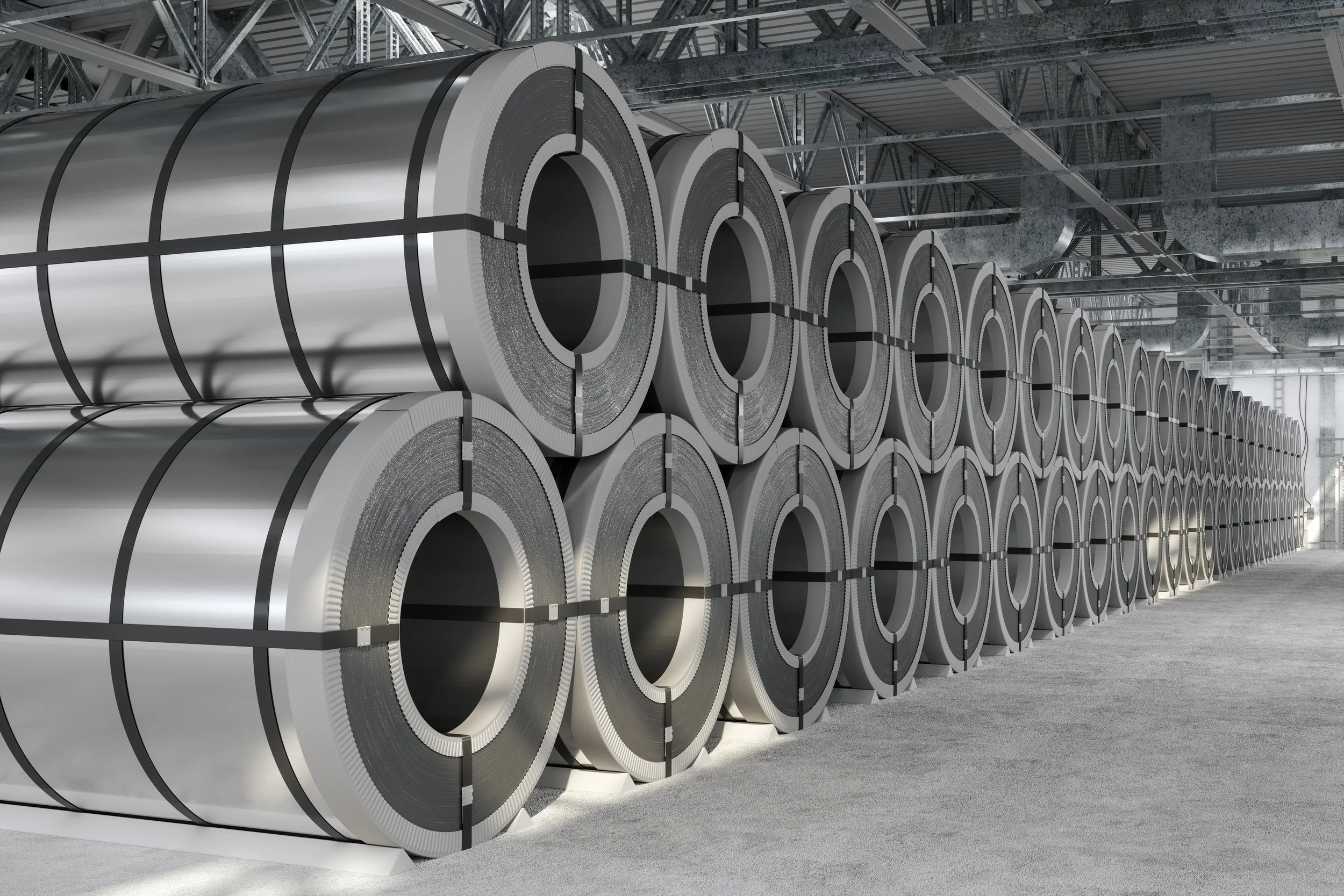 Indoor warehouse storing numerous large metal coils stacked in rows.