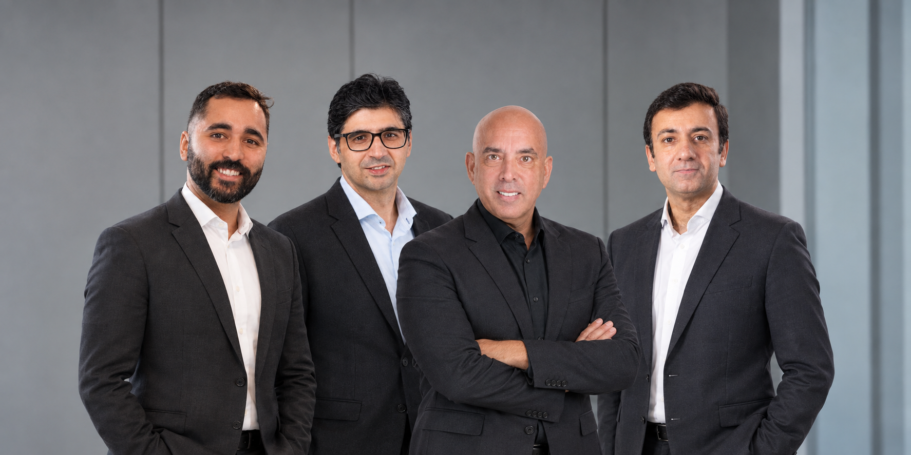 Four businessmen in dark suits posing together in an office setting.