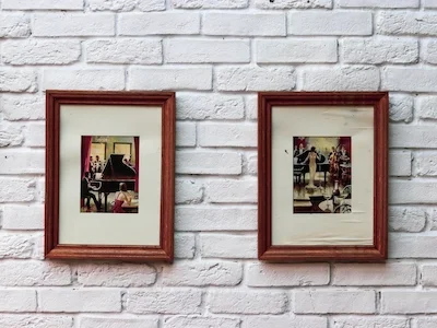 Two framed photos hanging on a white brick wall.