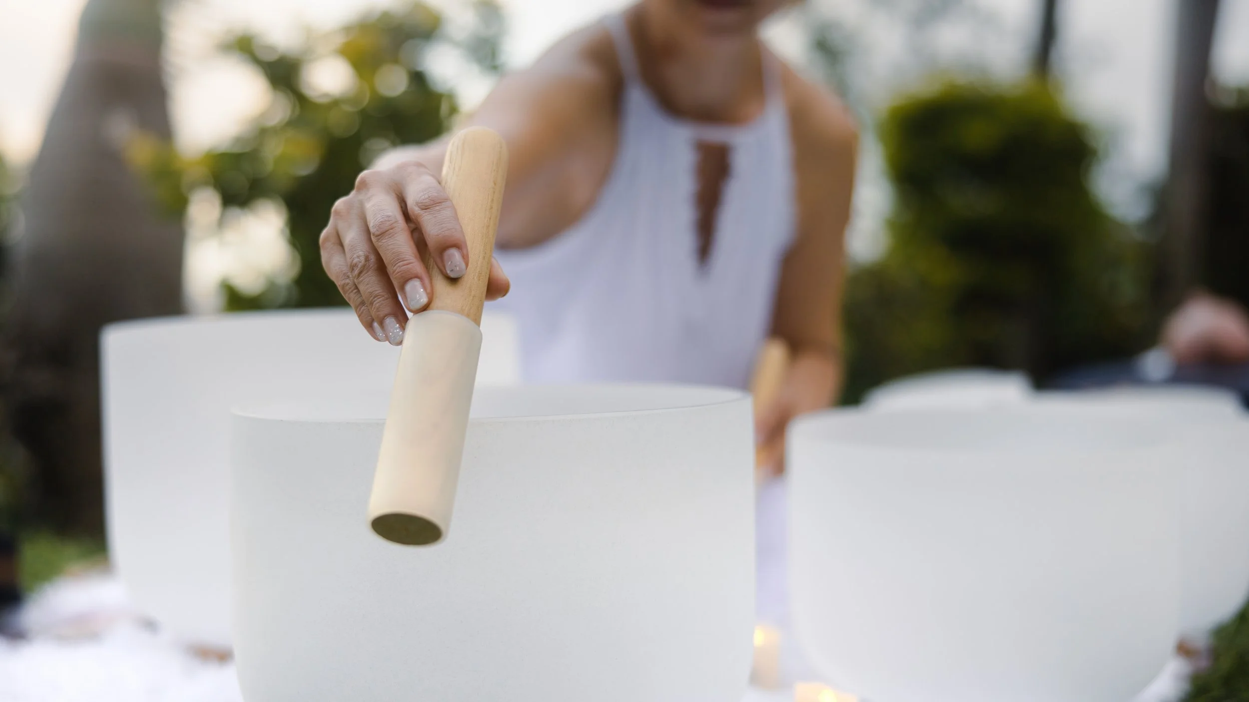 A woman in a white sleeveless top playing a crystal singing bowl. Schedule a Sound Bath session with Synergy Healing Arts in Og