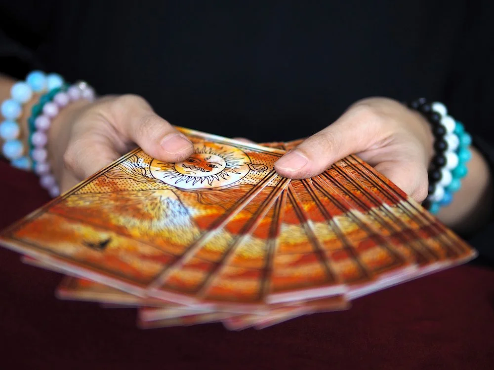 Person holding a fan with a sun and lion illustration, wearing beaded bracelets.  Book a Tarot Reading at Synergy Healing Arts in Ogden, Utah.