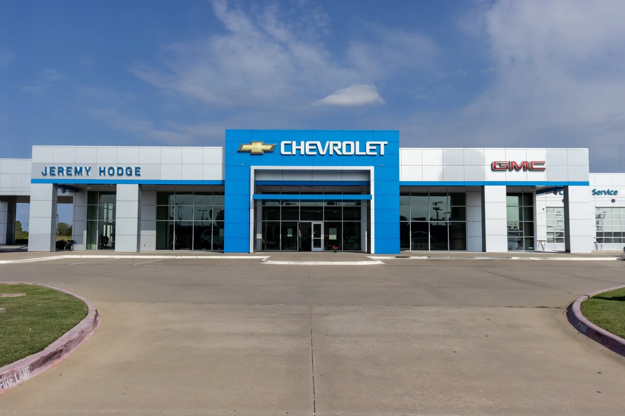 Exterior of Jeremy Hodge Chevrolet dealership with Chevrolet, GMC, and Chevrolet signages, under a partly cloudy sky.