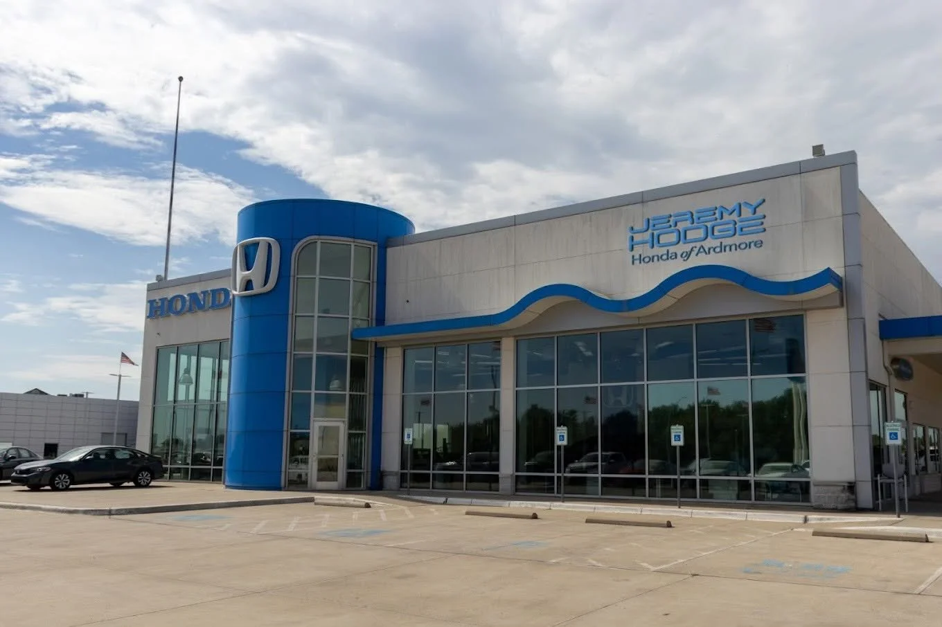 Exterior of a Honda car dealership named Jeremy Honda of Ardmore, with parking spaces and cars in front.
