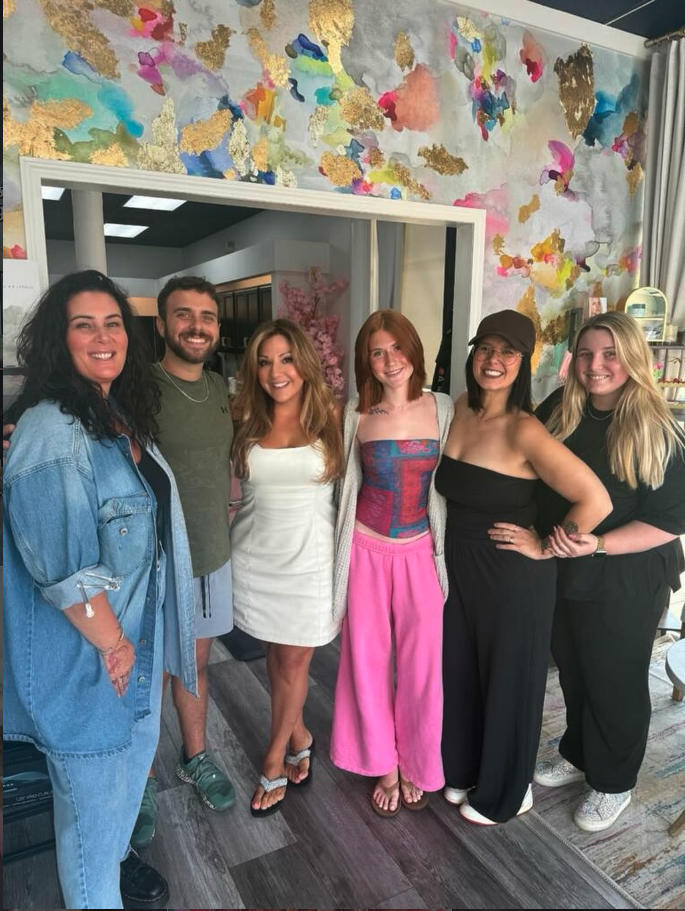 Group of six people standing inside a room with colorful abstract wallpaper, smiling for the camera.