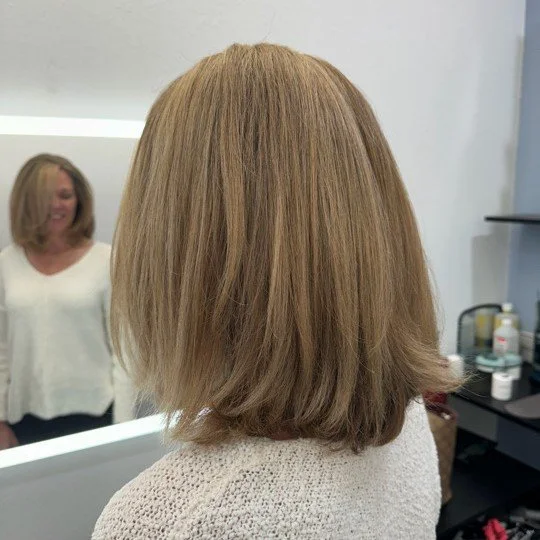 Side view of a woman with shoulder-length light brown hair in a hair salon.
