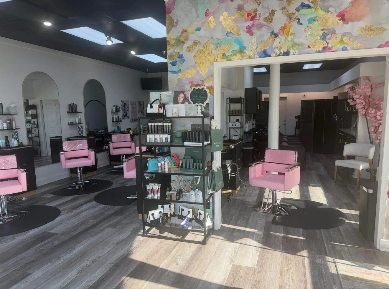 Interior of a hair salon with pink chairs, hair care products on display, and a floral mural on the wall.