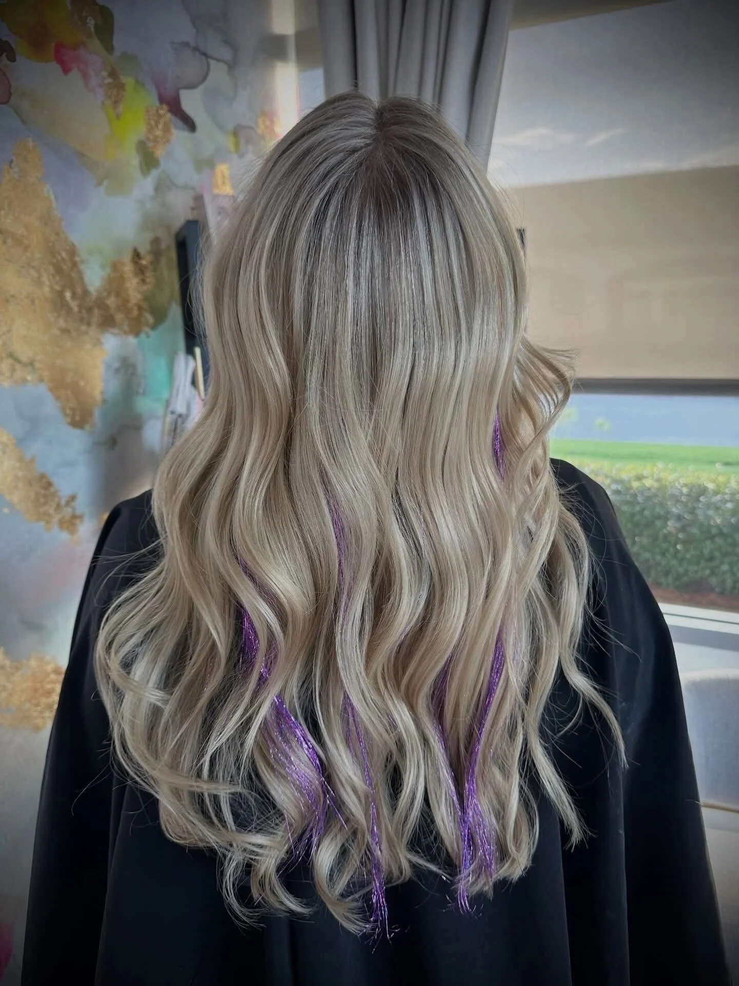 Long blonde hair with purple streaks styled in loose waves.