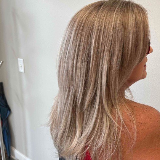 Side view of a woman with long, blonde hair and a red top, standing indoors near a white wall.