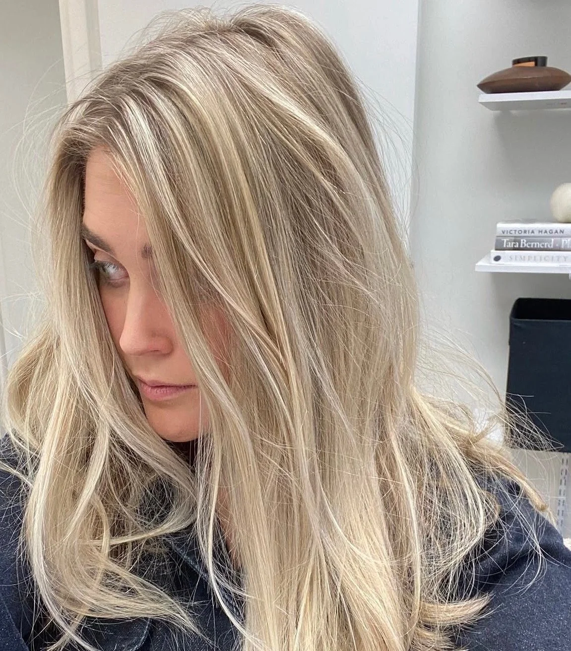 A woman with long, blonde, wavy hair looking to her left in an indoor setting.