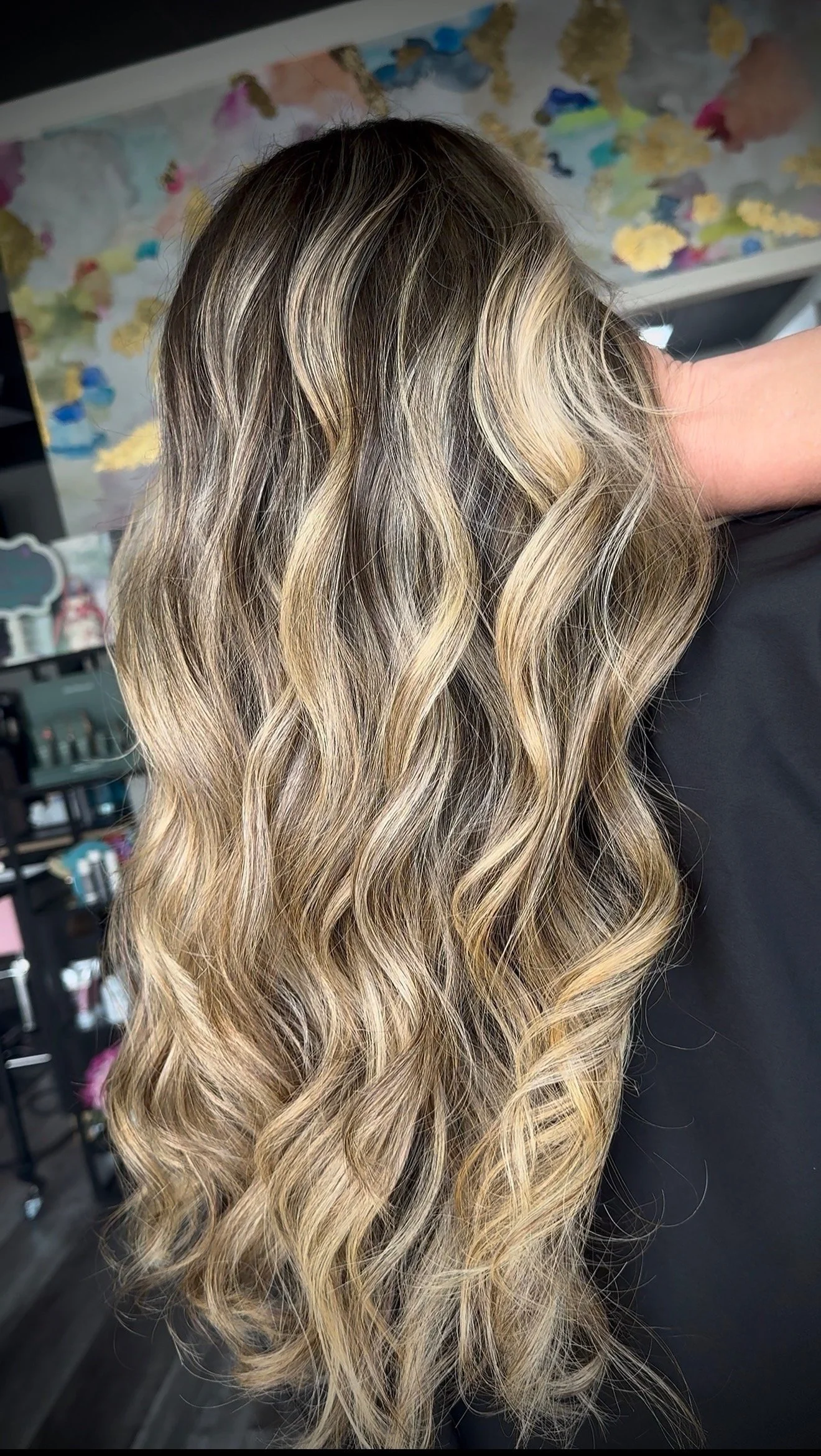 Close-up of long, wavy hair with blonde highlights and darker roots, styled in loose waves.