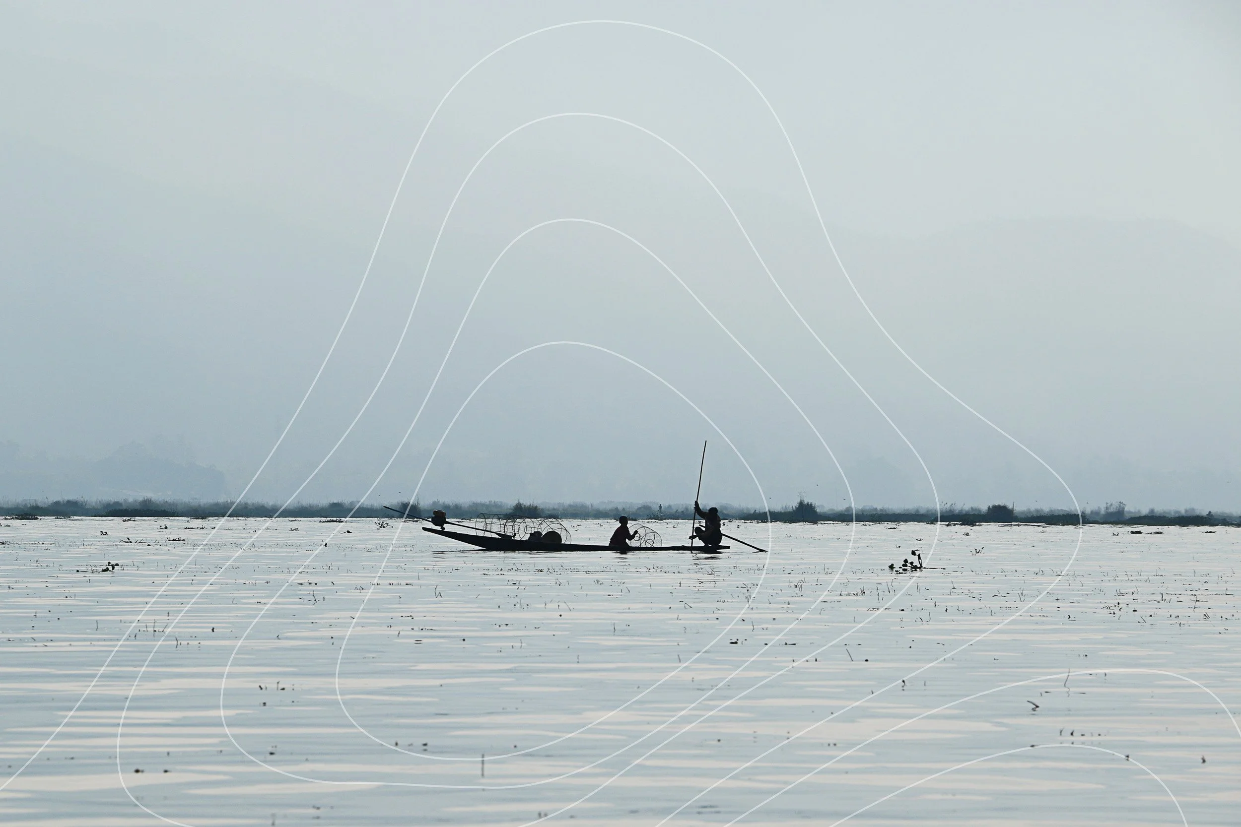 Two fishermen with conical nets on a boat crossing still water at dawn