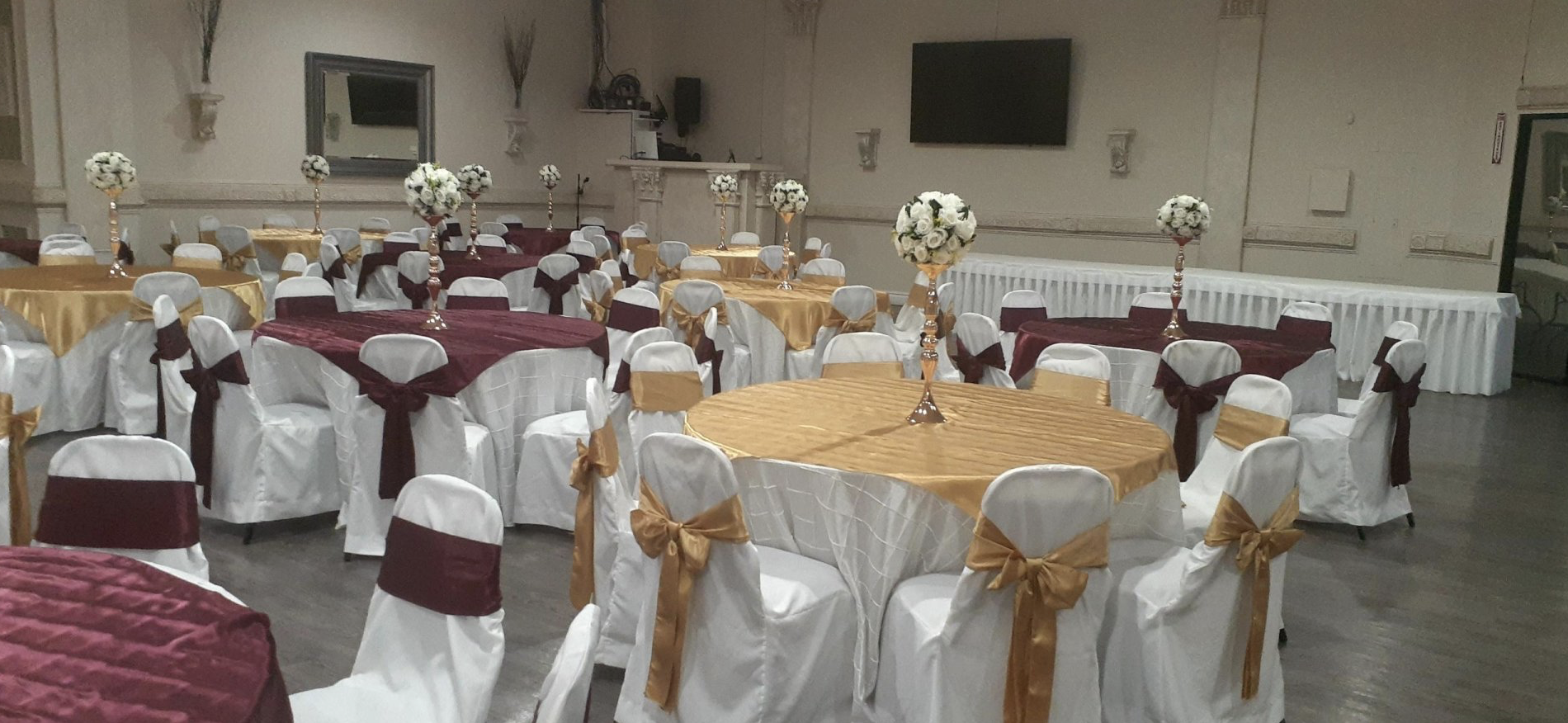 Reception setup featuring round tables, white chair covers, gold accents, and elegant centerpieces.
