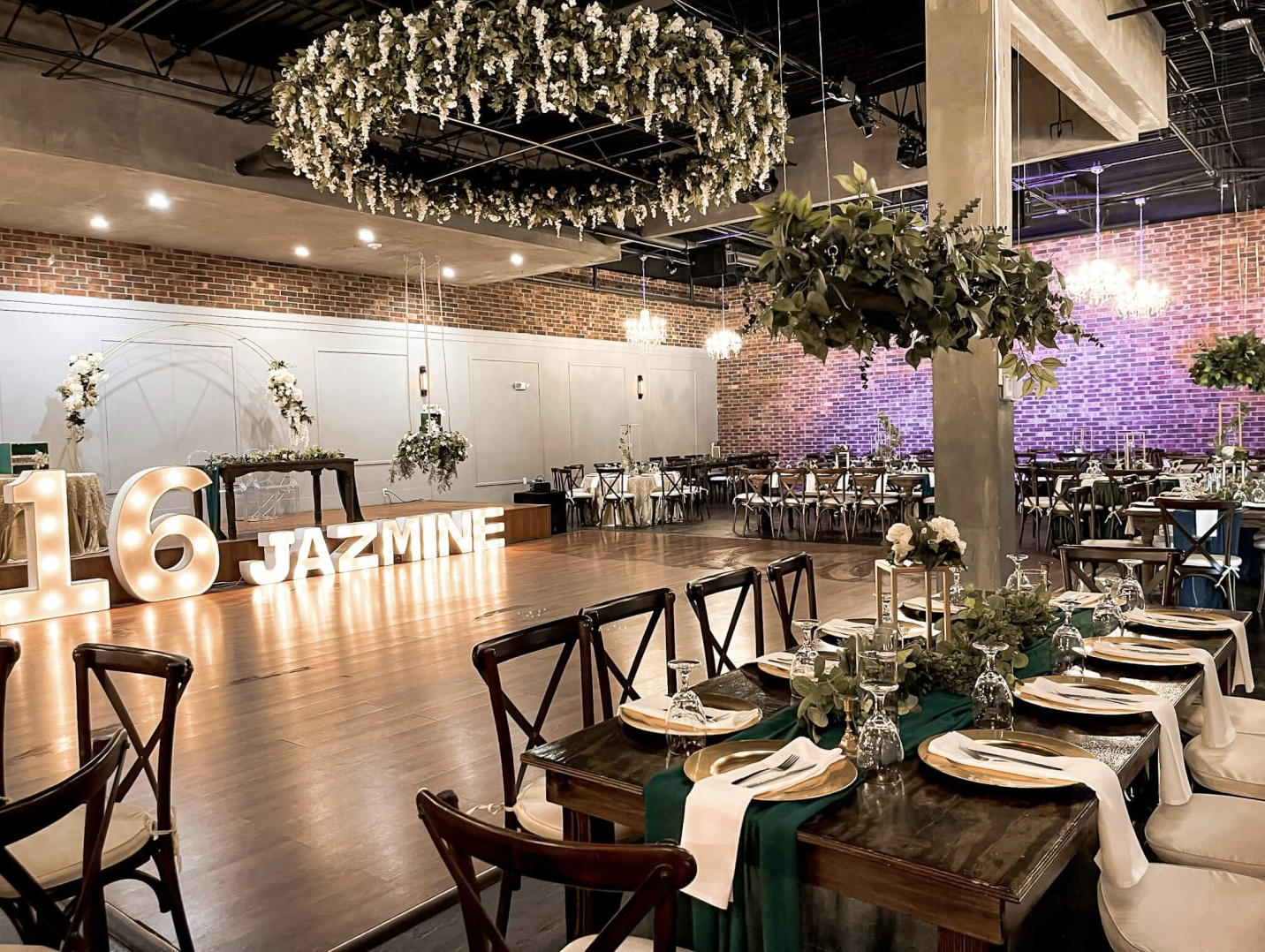 Elegant reception setup featuring round tables, white chair covers, gold accents, greenery, and floral centerpieces.