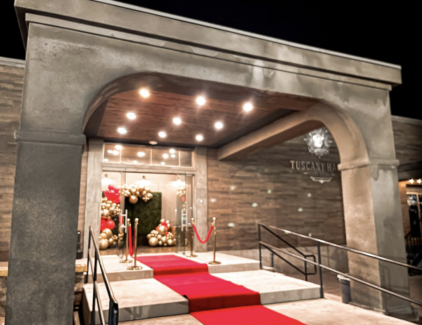 Stone entrance decorated with a red carpet, floral arrangements, and warm overhead lighting.