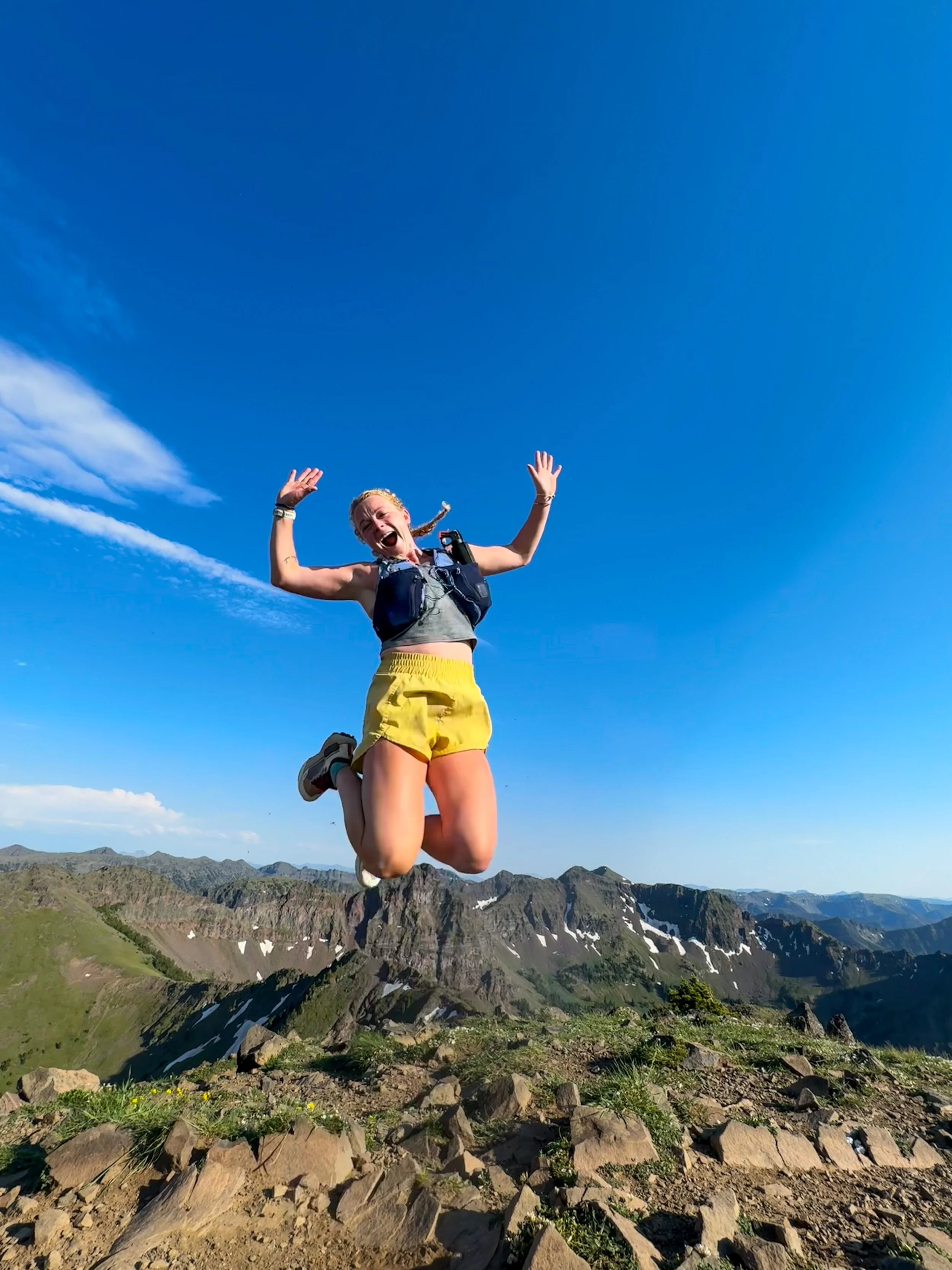 A woman jumping in the air with mountains and blue sky in the background.
