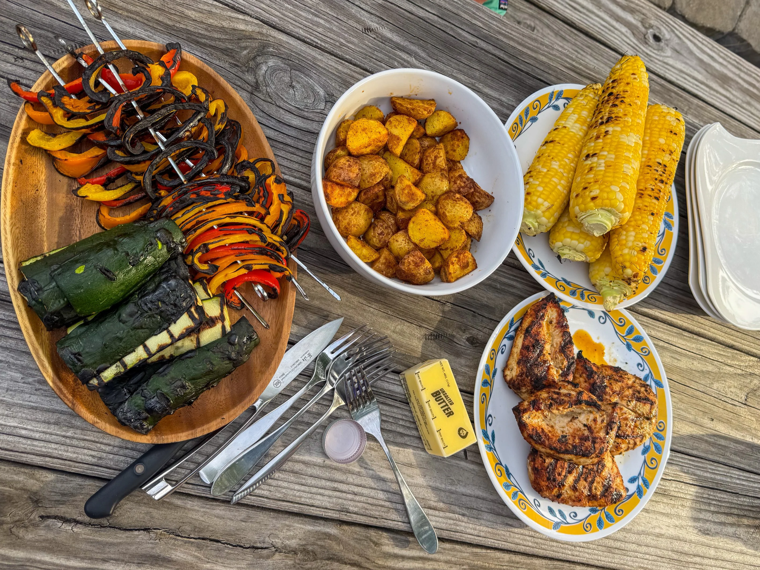 Grilled vegetables skewers, roasted potatoes, and grilled corn on a table.