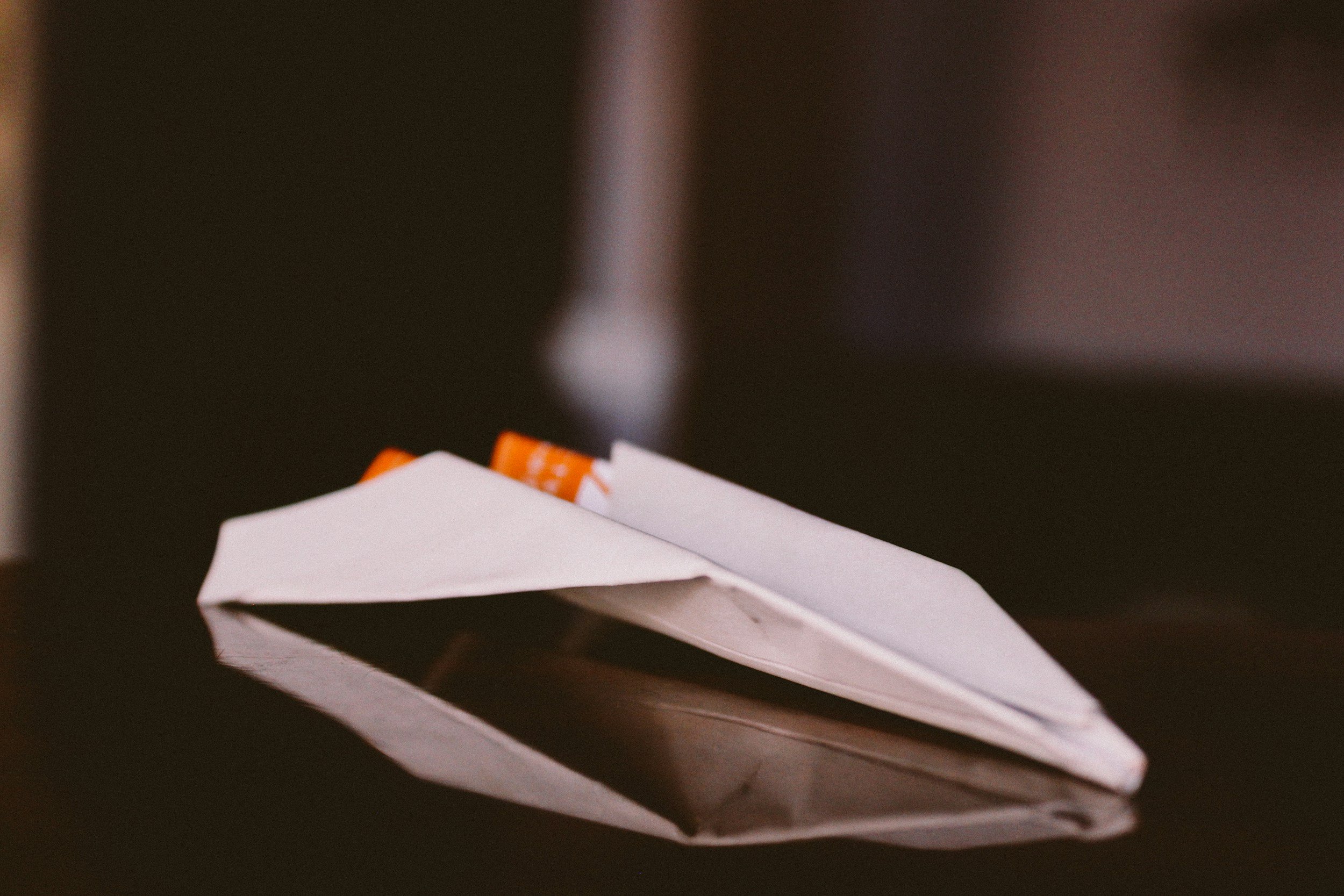 Close-up of a white paper airplane with a partially visible orange and white sticker on it, against a dark background.
