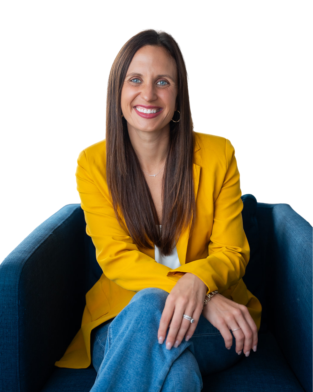 A woman with long brown hair and blue eyes, smiling, wearing a yellow blazer, seated on a dark blue sofa.