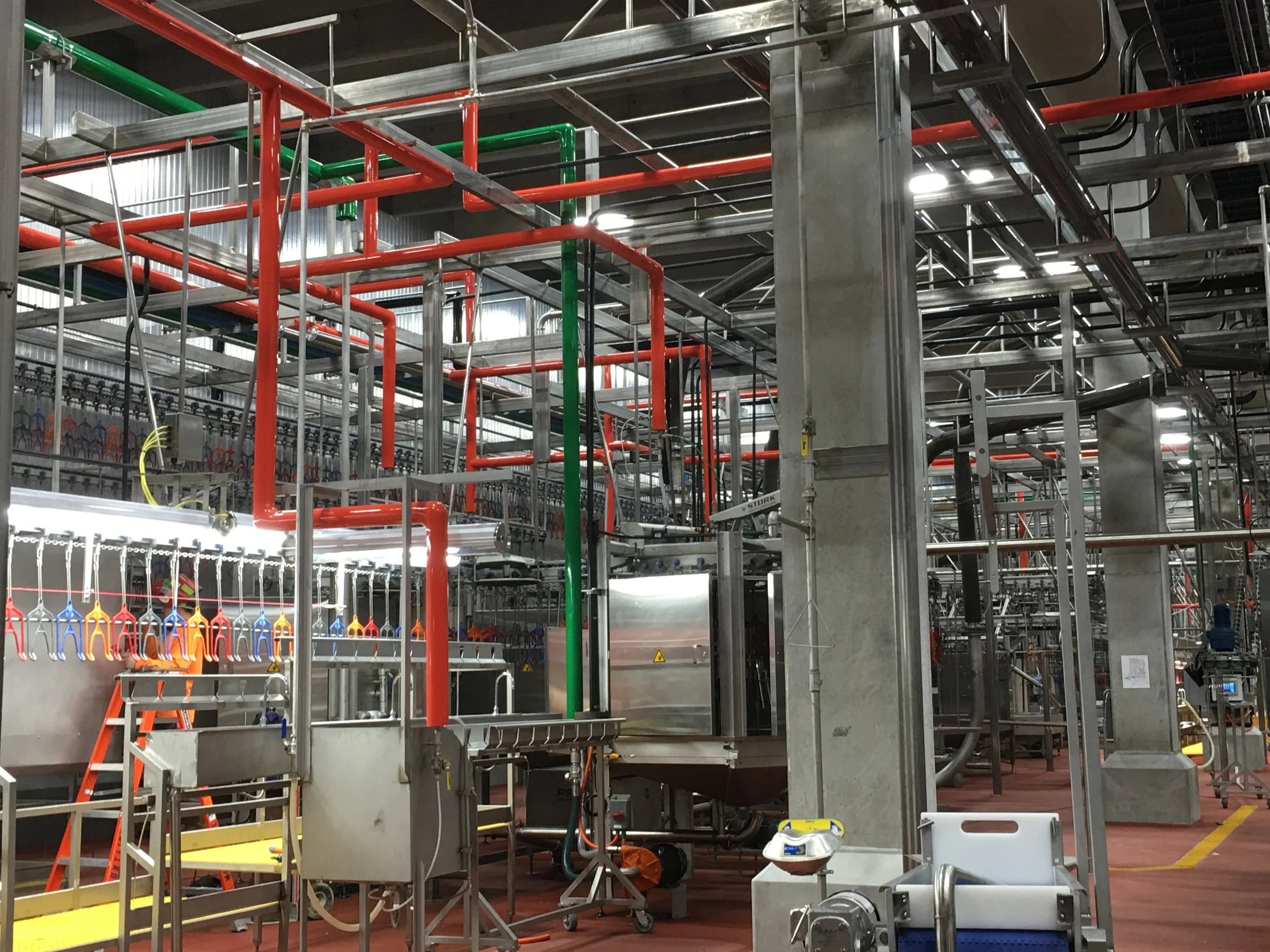 Industrial construction site with metal scaffolding, pipes, and equipment in a factory or large facility.
