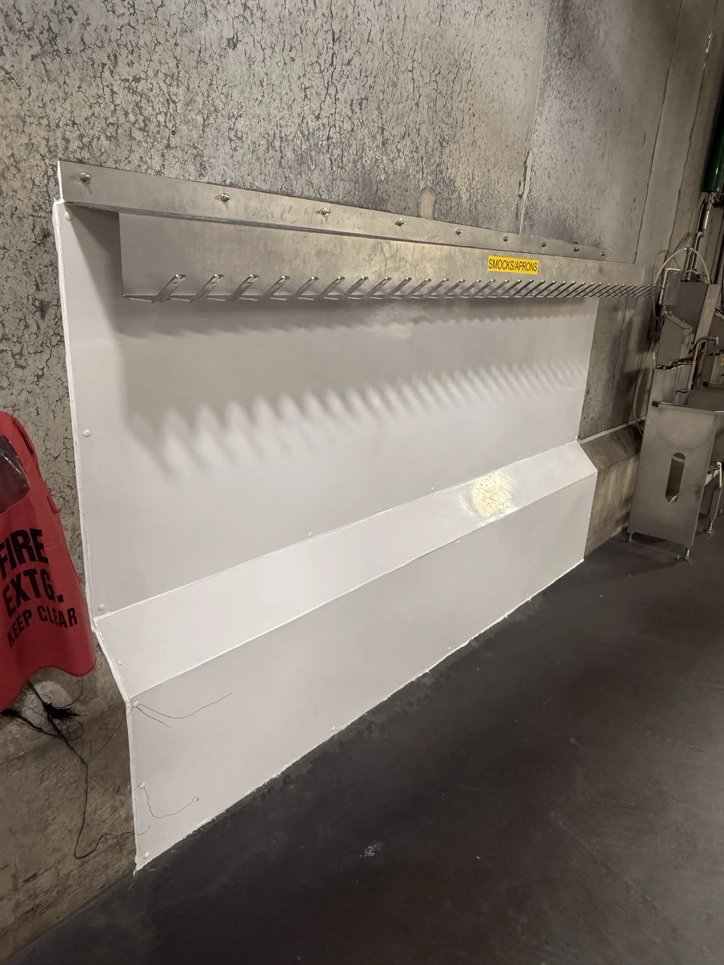 A metal sconce with hooks mounted on a textured wall, labeled 'Smooch/Aprons' with a yellow sticker.