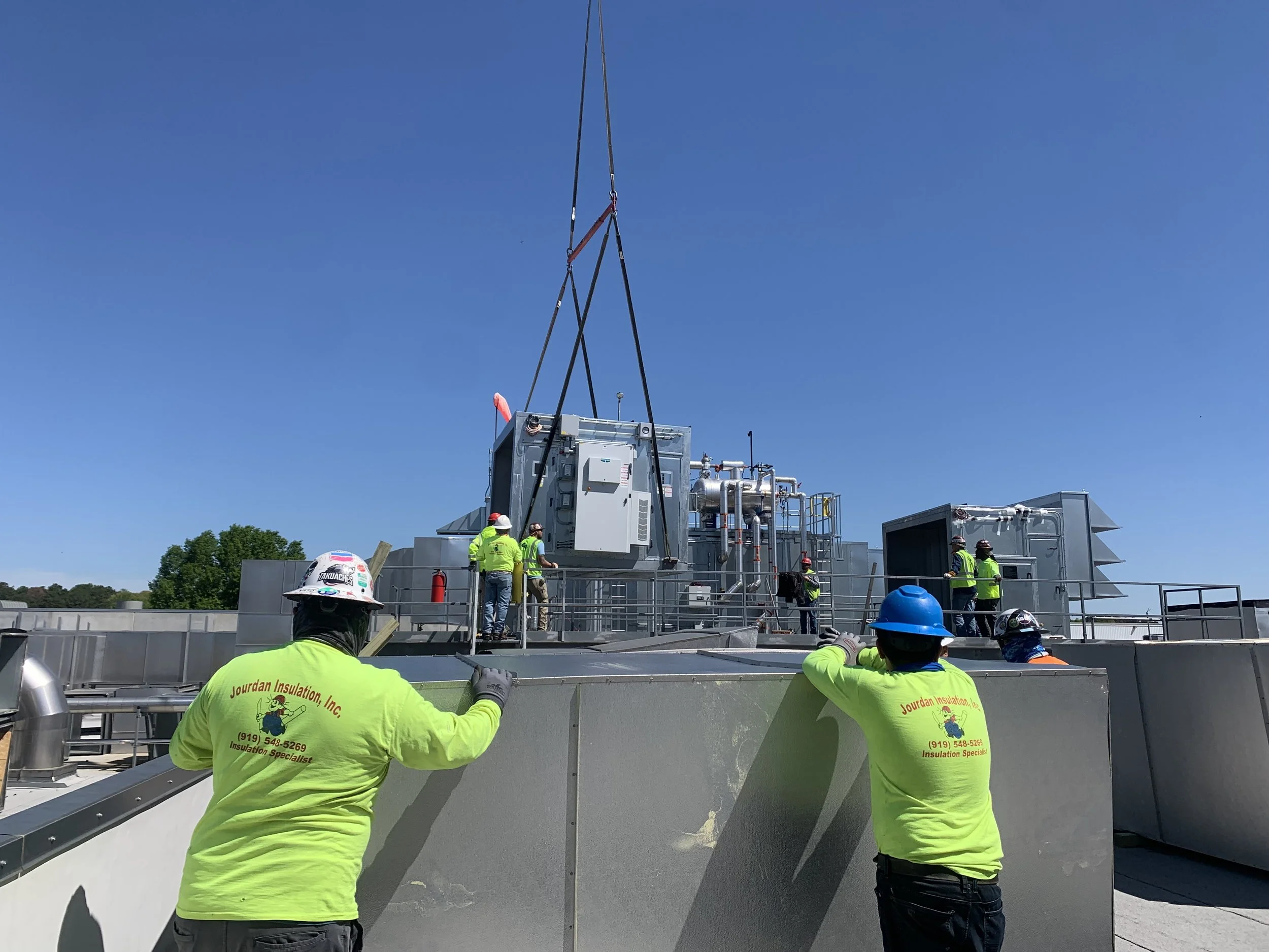 Workers in bright yellow shirts with company logo working on rooftop HVAC system against blue sky