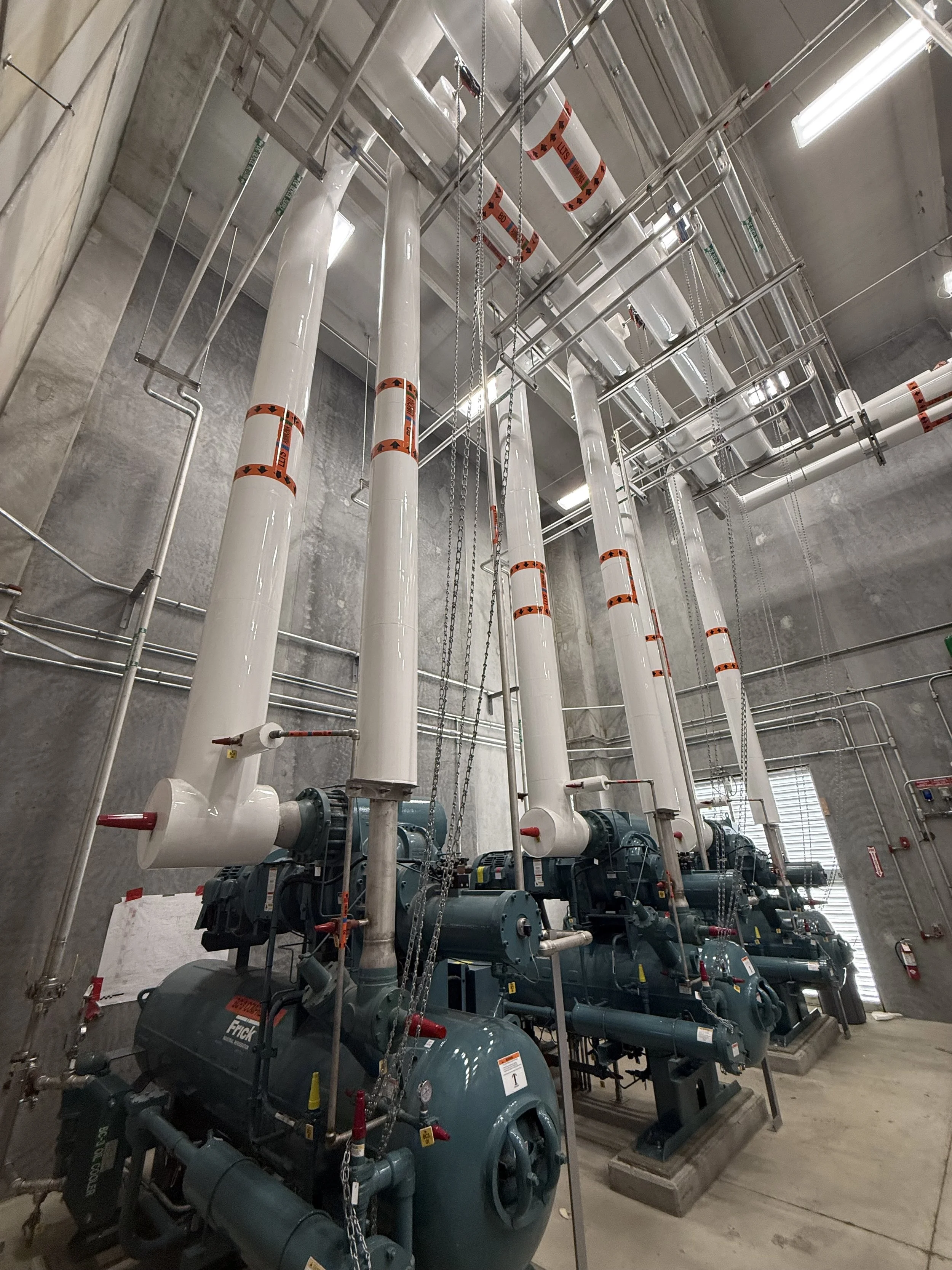 Industrial HVAC system with large pipes, pumps, and electrical components in a concrete room.