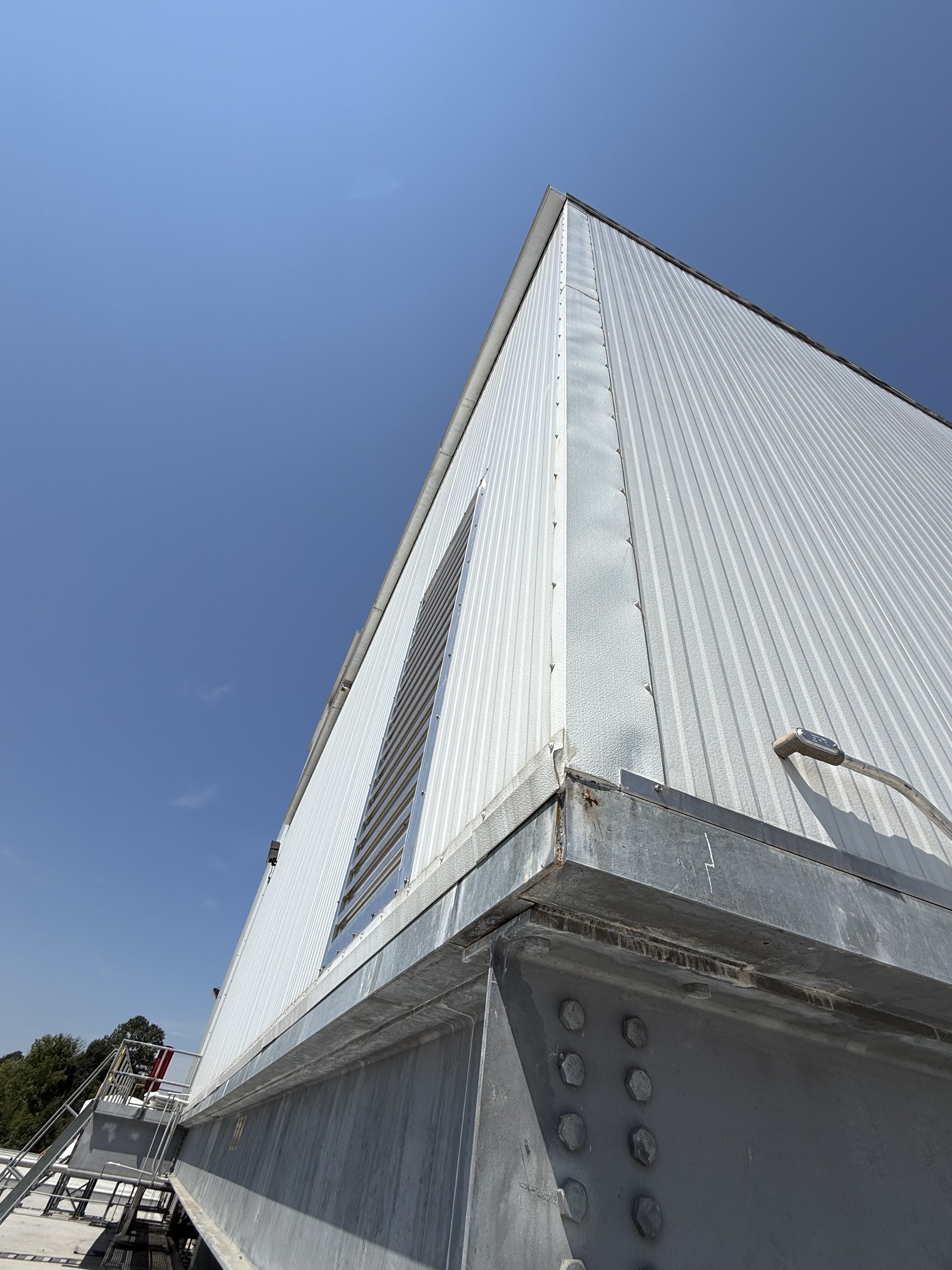 Close-up view of a modern industrial building with metallic siding and bolted metal panels, under a clear blue sky.